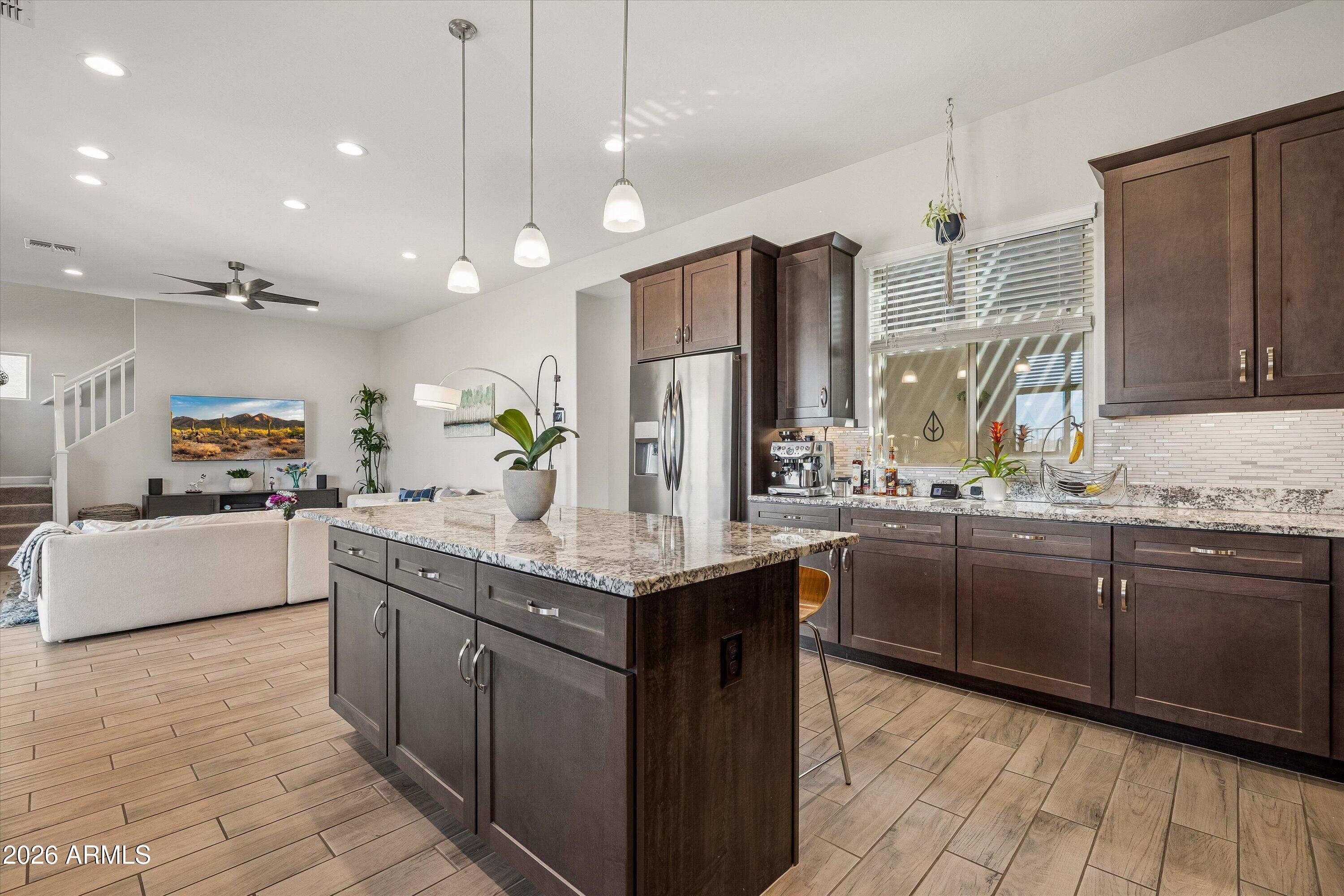 Open-plan kitchen with dark cabinets, stainless steel appliances, and a large granite-topped island beside the living area.