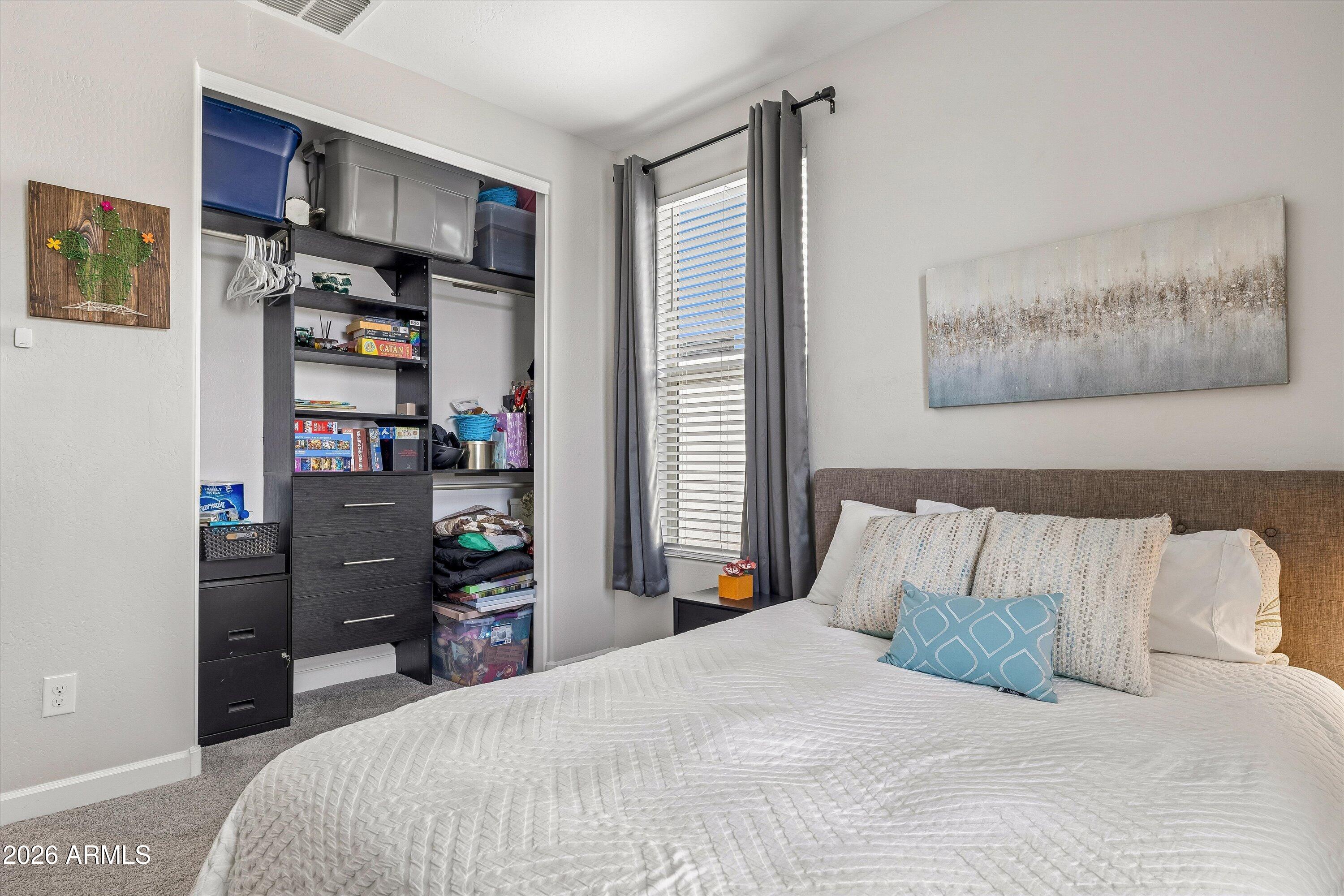 Furnished bedroom with white bedding, blue accent pillows, and an open, organized closet.