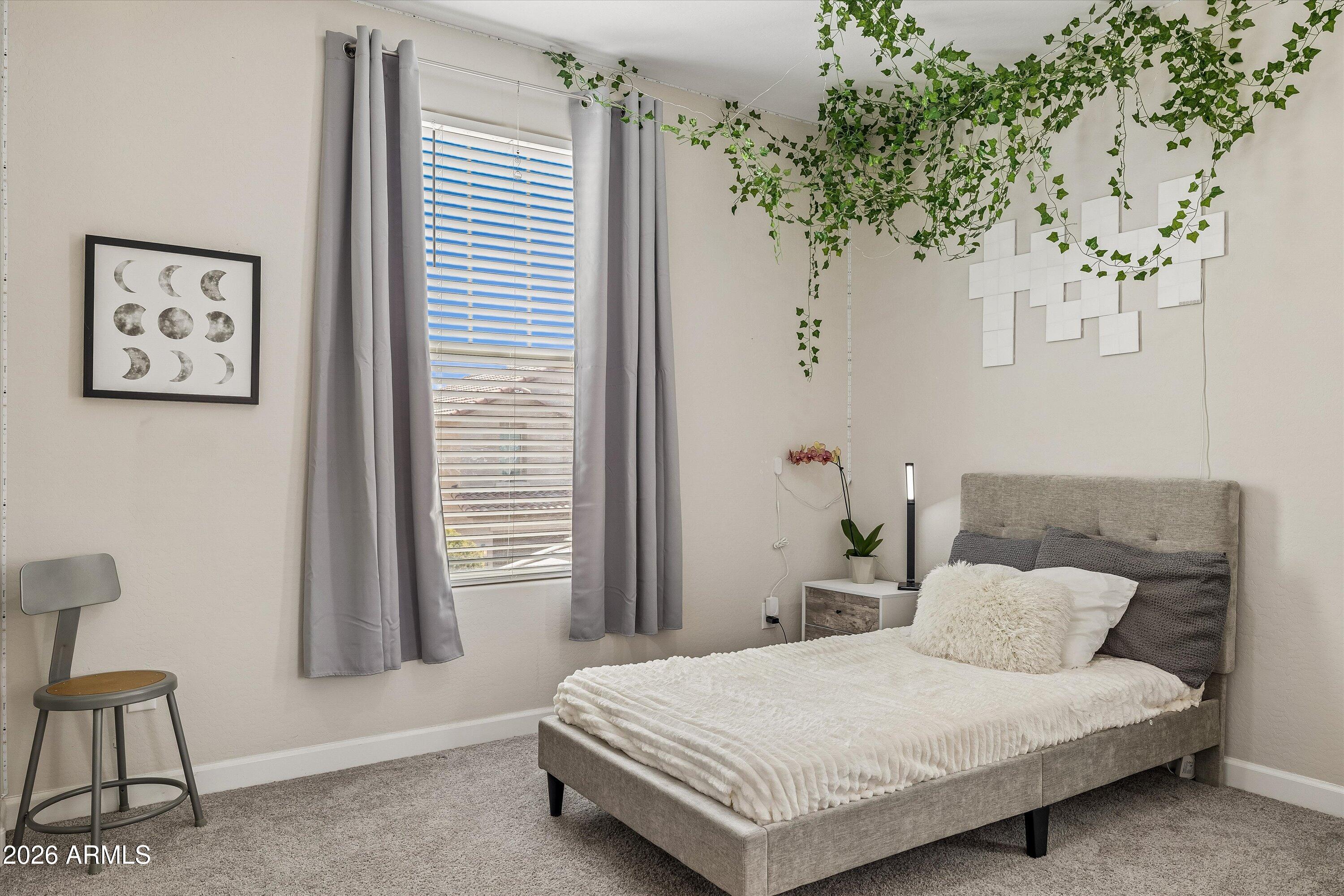Bedroom with a gray upholstered bed, white bedding, gray curtains, and trailing vines overhead.