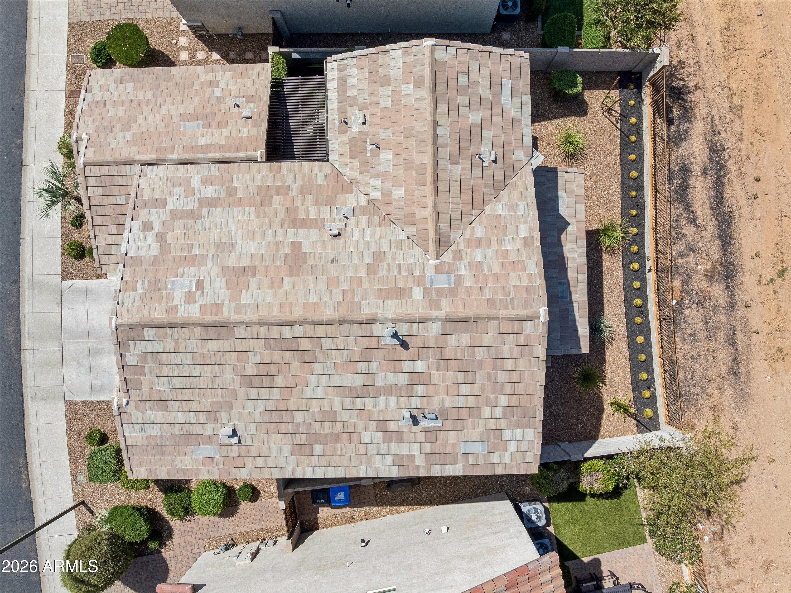 Aerial view of a tan tiled roof, landscaped yard, artificial turf, and adjacent undeveloped lot.