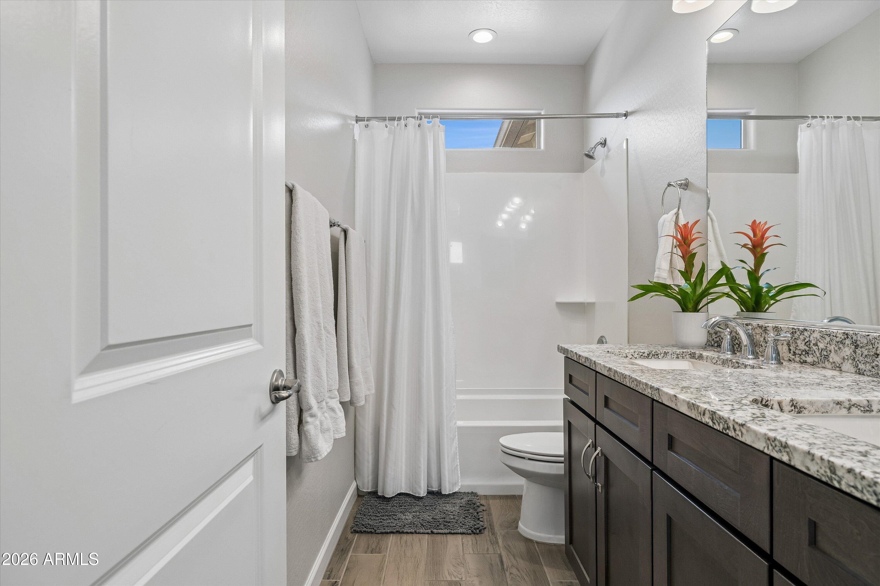 Bathroom with a granite double vanity, dark cabinets, and potted plants beside a curtained shower.