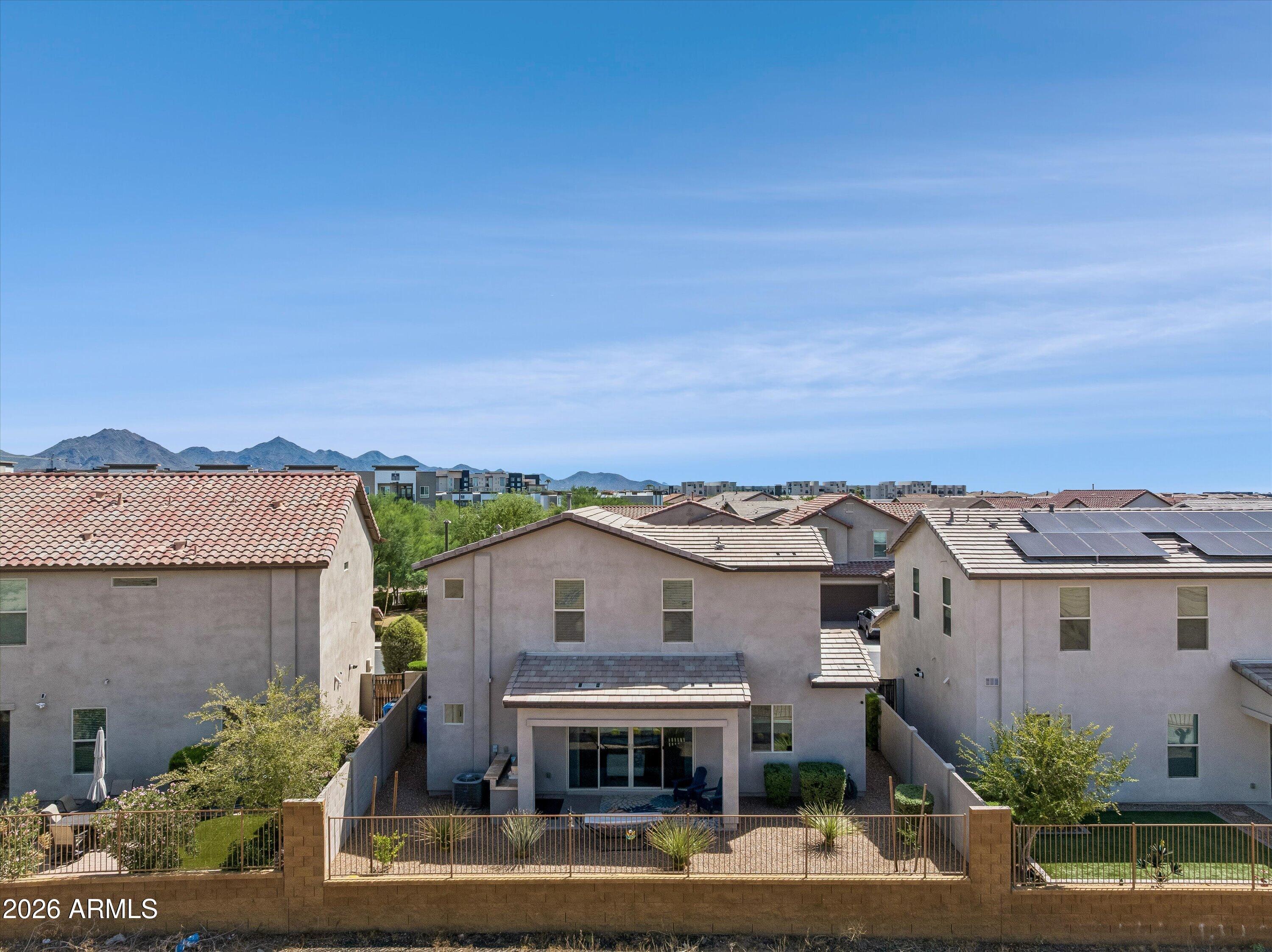Rear of a two-story home with a covered patio, fenced yard, and mountains beyond.