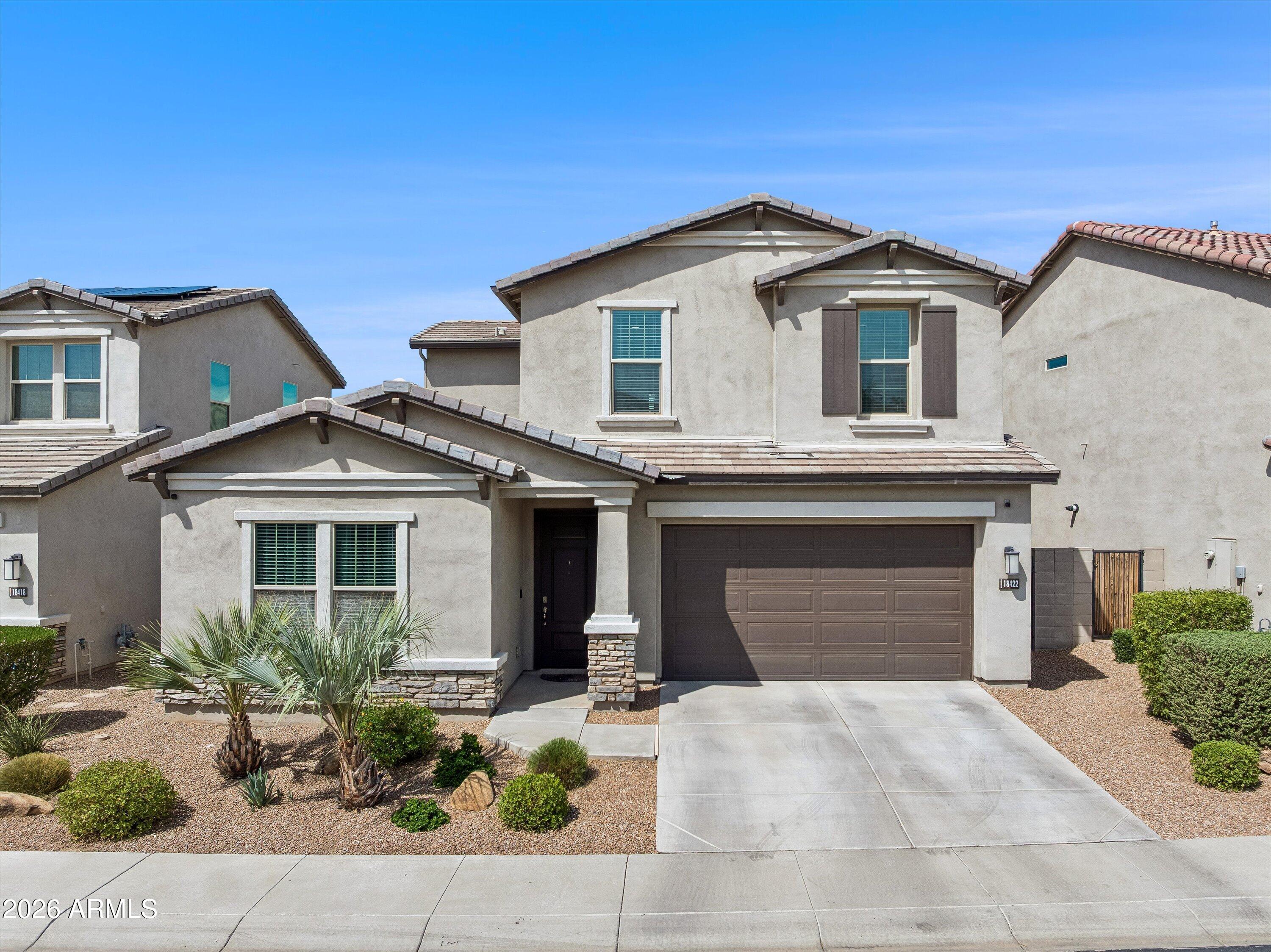 Two-story stucco home with a dark double garage, wide driveway, and desert landscaping.