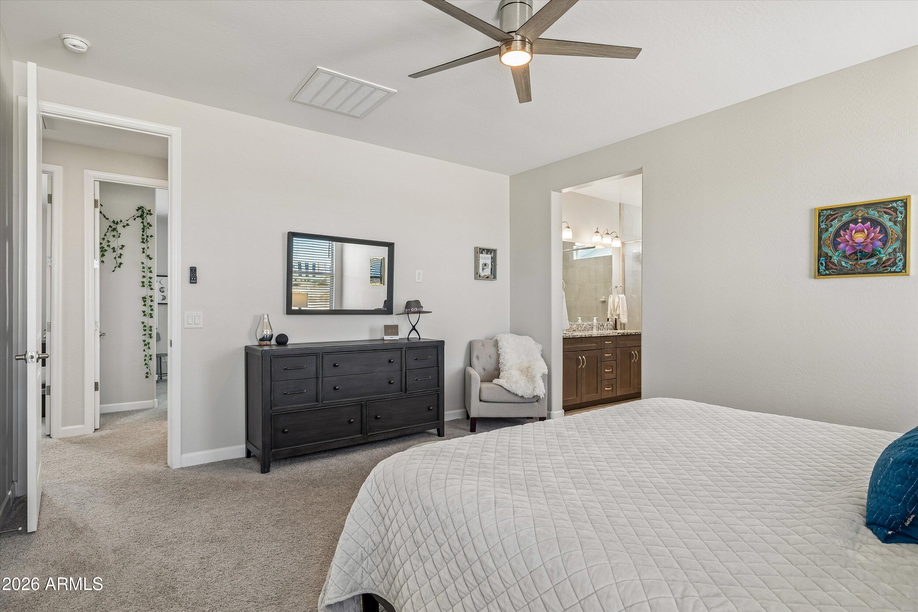 Furnished bedroom with an ensuite vanity, dark dresser, ceiling fan, and carpeted floor.