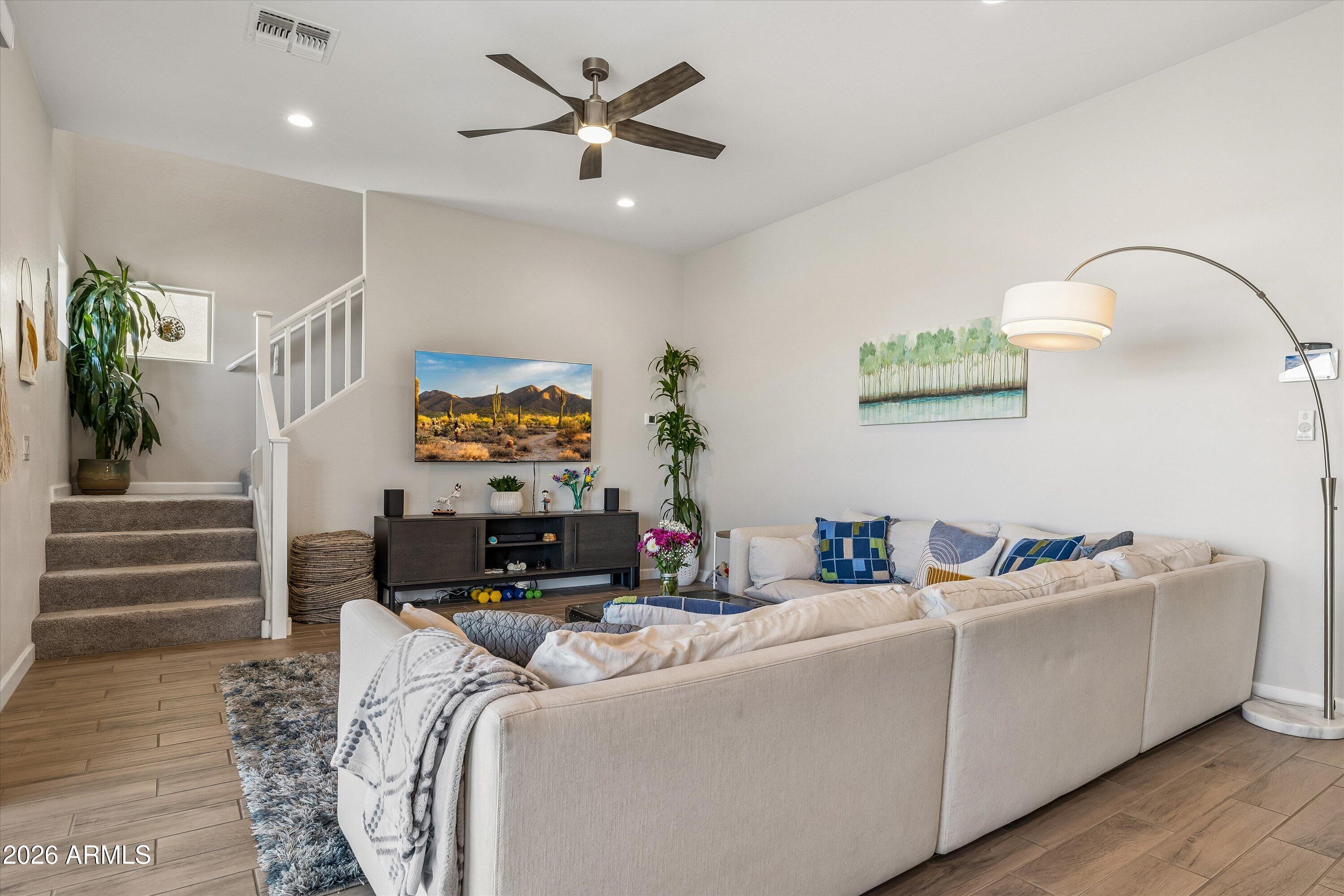 Furnished living room with a cream sectional, carpeted staircase, and desert landscape artwork.