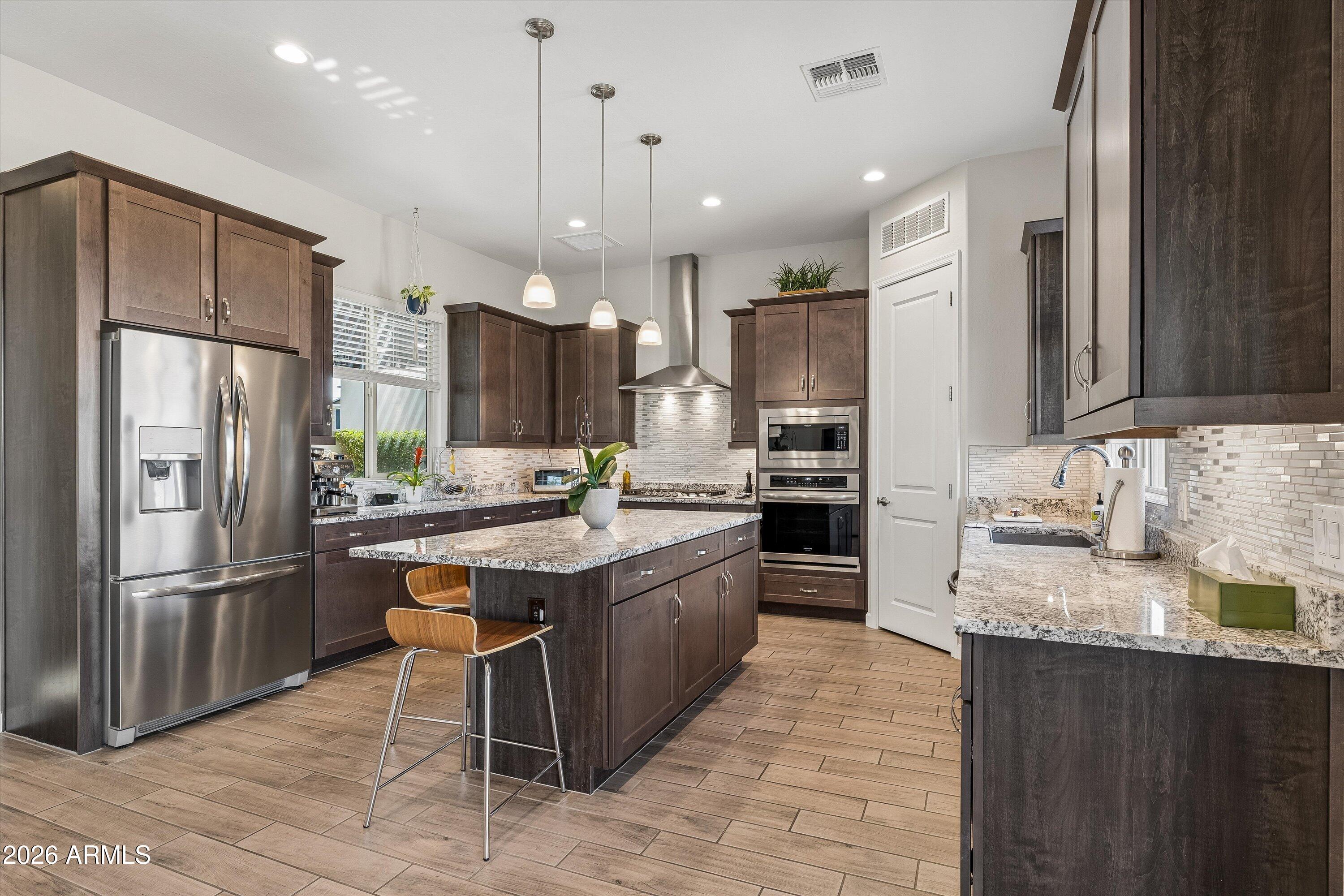 Kitchen with dark wood cabinets, granite island, stainless steel appliances, and pendant lighting.