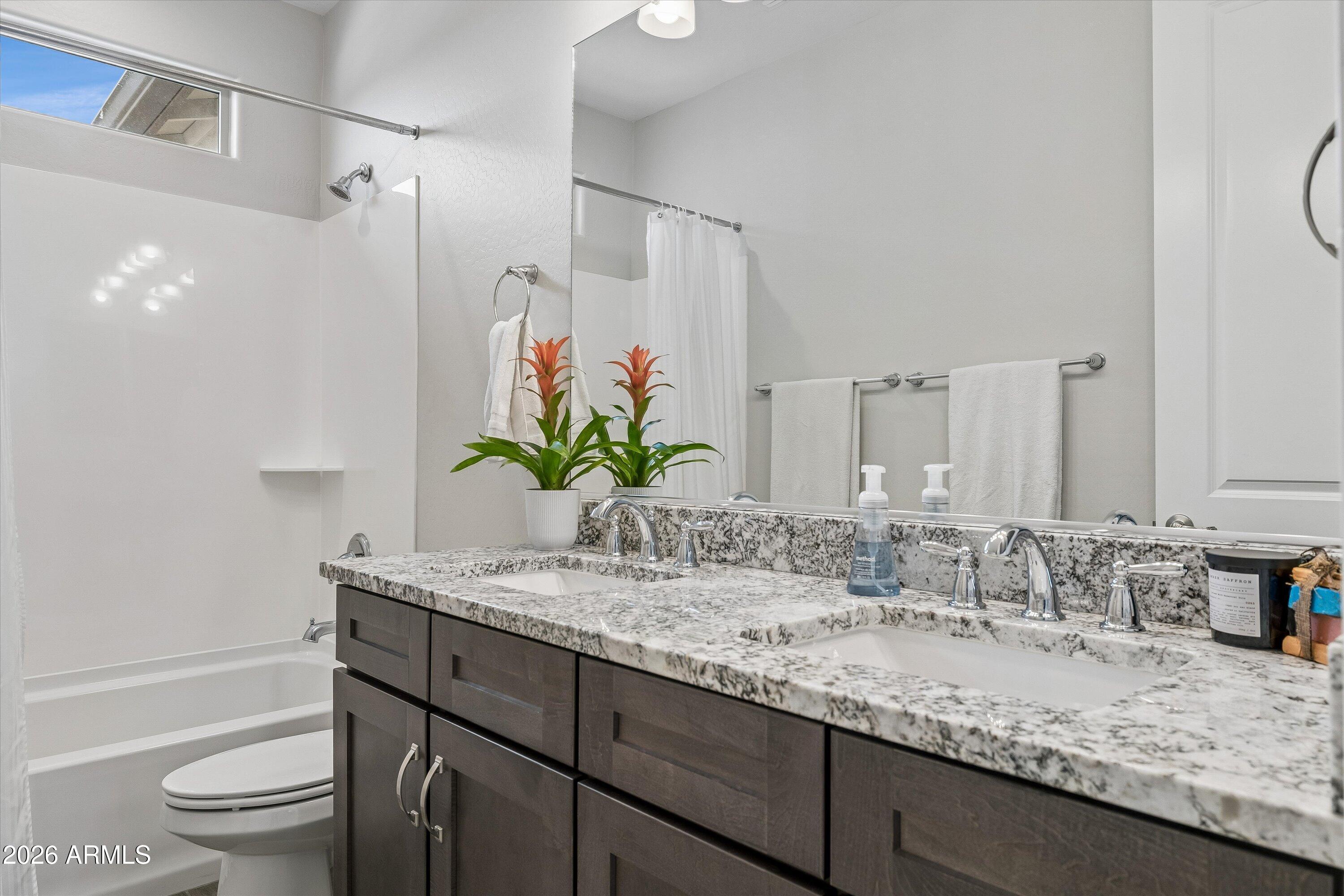 Bathroom with a double-sink granite vanity and bathtub beneath a high window.