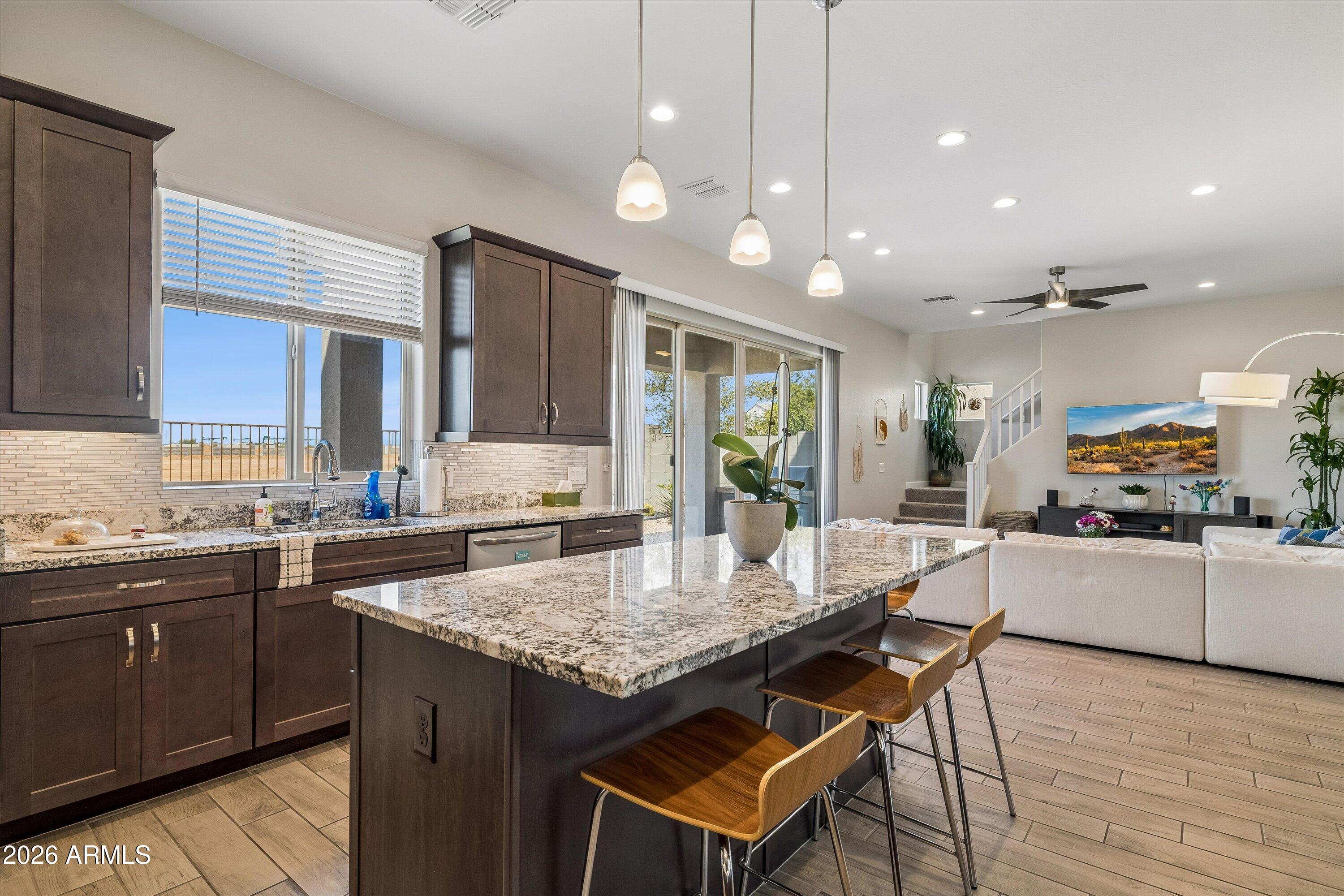 Kitchen with a large granite island, dark wood cabinets, and an adjoining living area.