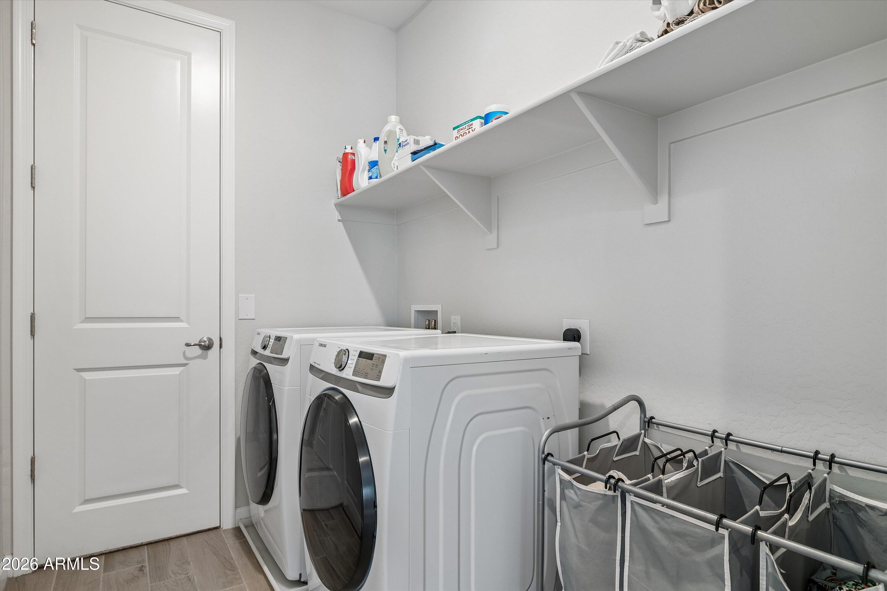 Laundry room with front-loading washer and dryer, storage shelves, and a rolling laundry sorter.