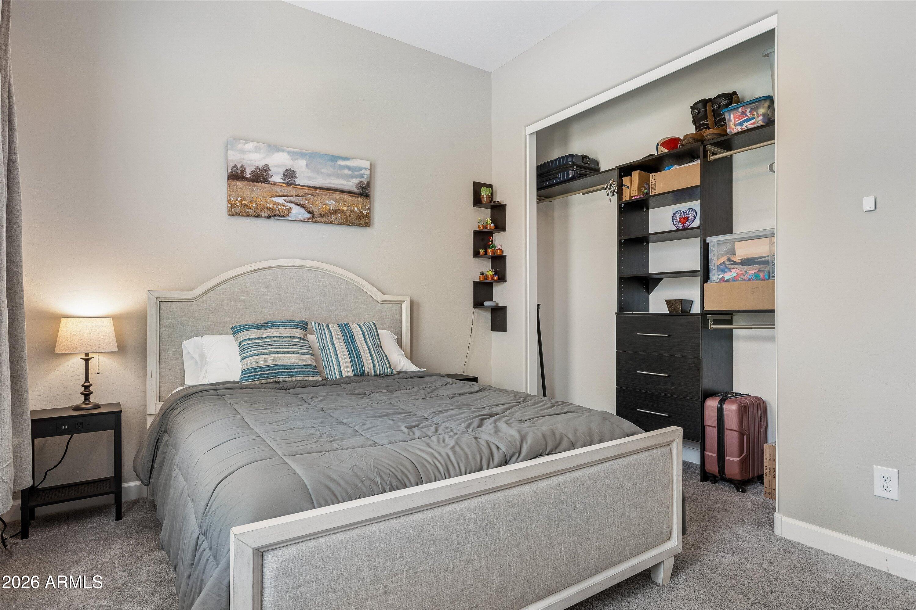 Furnished bedroom with a gray upholstered bed and an organized walk-in closet with dark shelving.