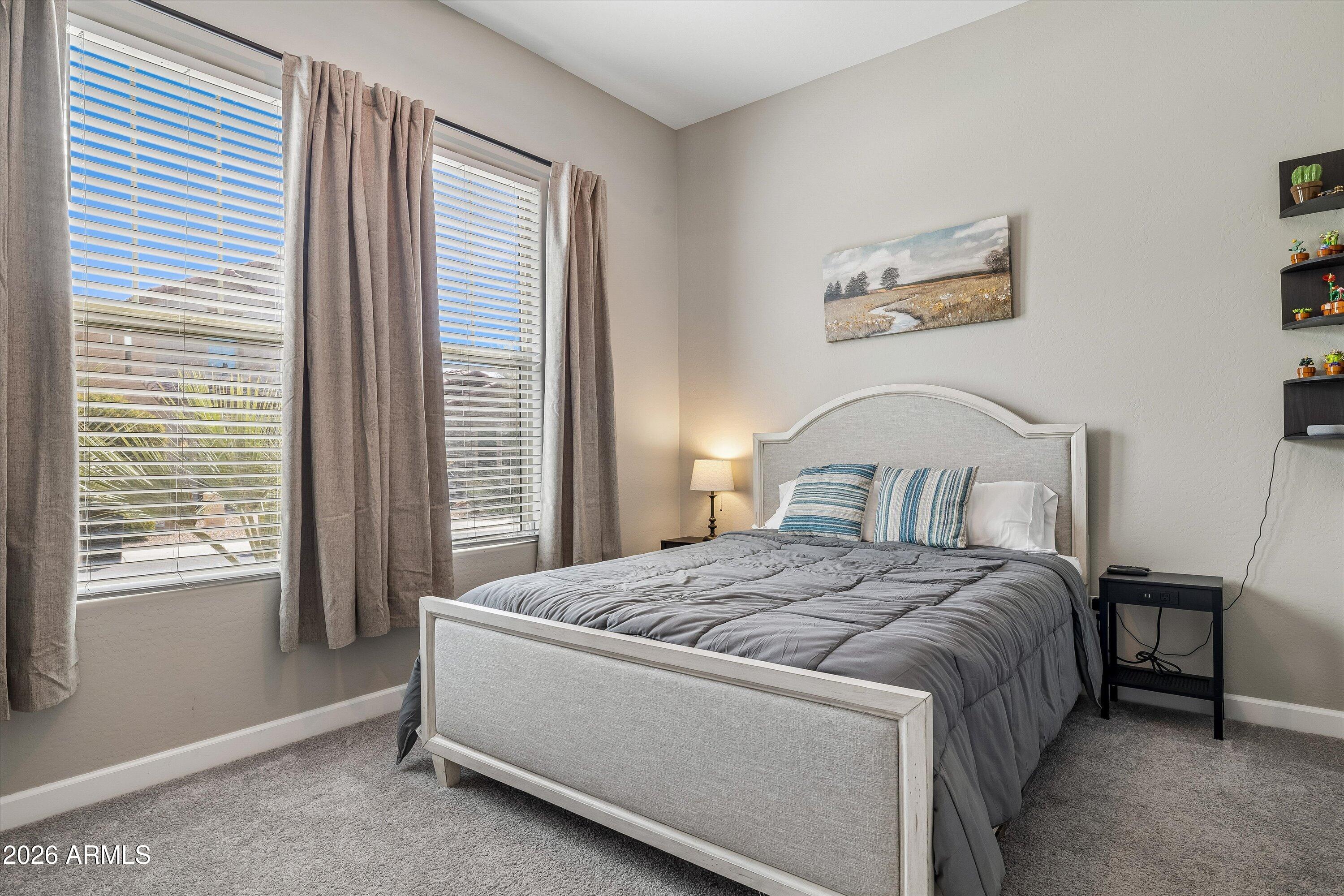 Furnished bedroom with a gray-covered bed, blue striped pillows, and two curtained windows.