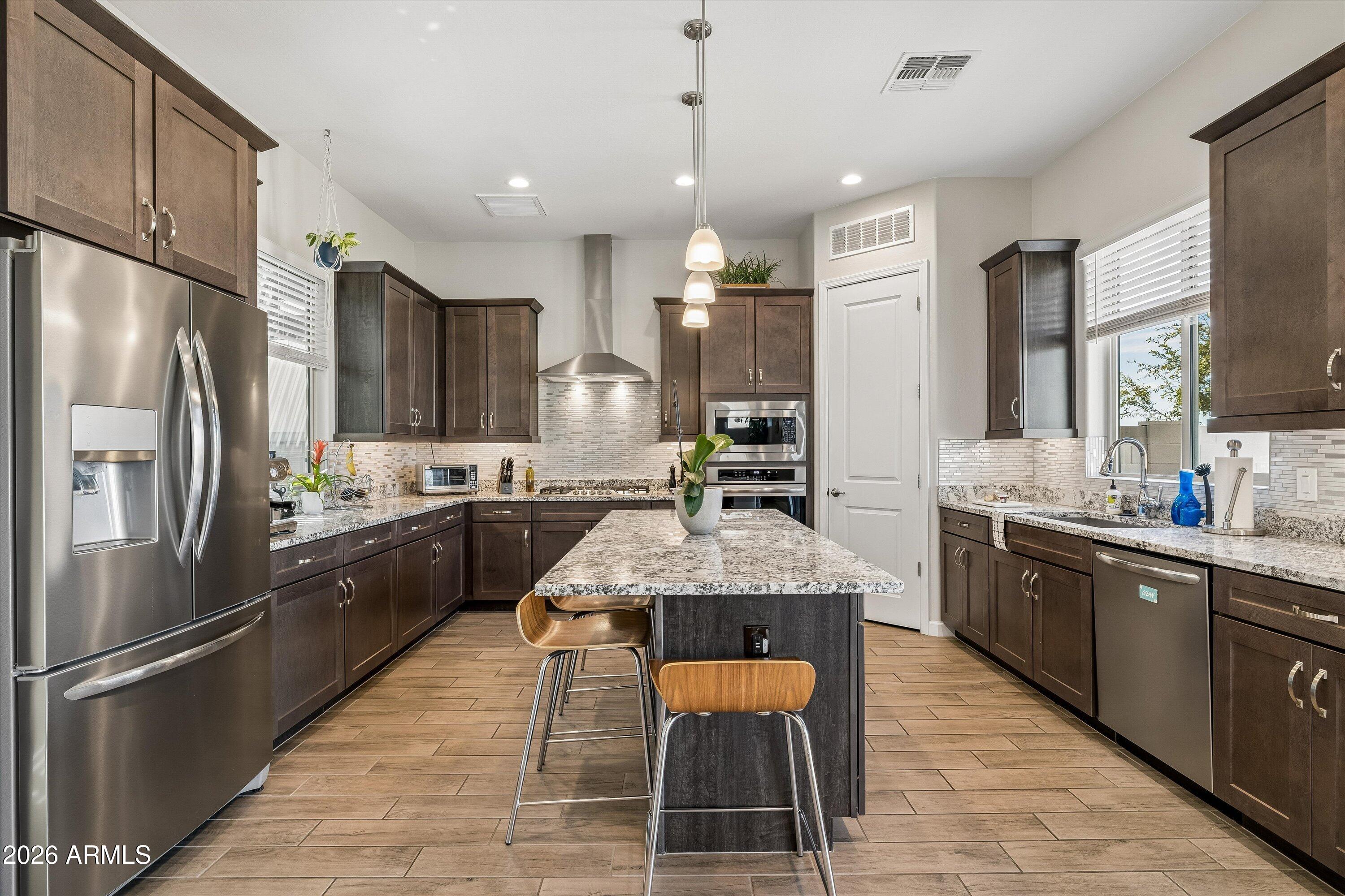 Kitchen with dark wood cabinets, stainless steel appliances, and a large granite island with two bar stools.