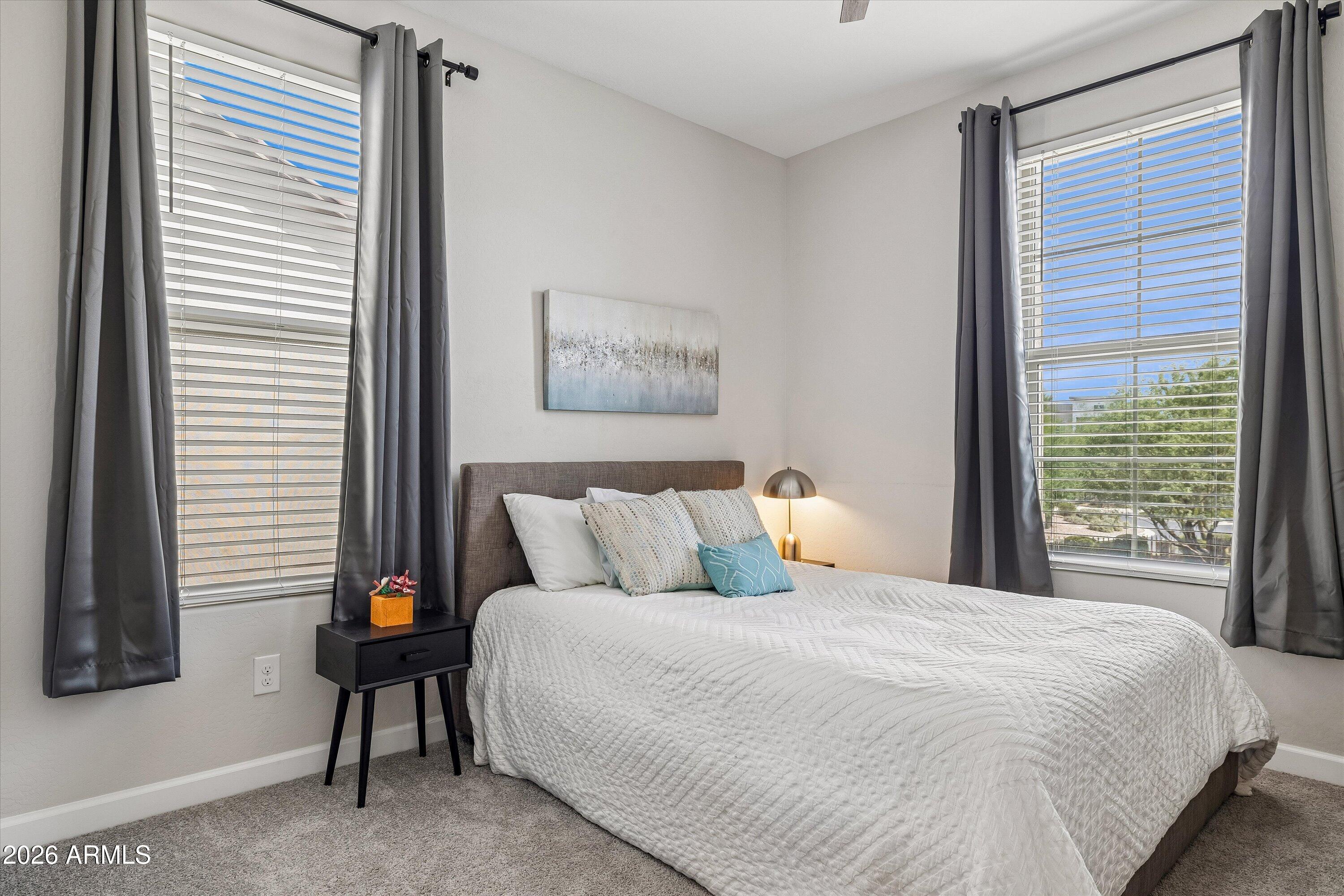 Bedroom with a white-quilted bed, gray curtains, and two large windows.