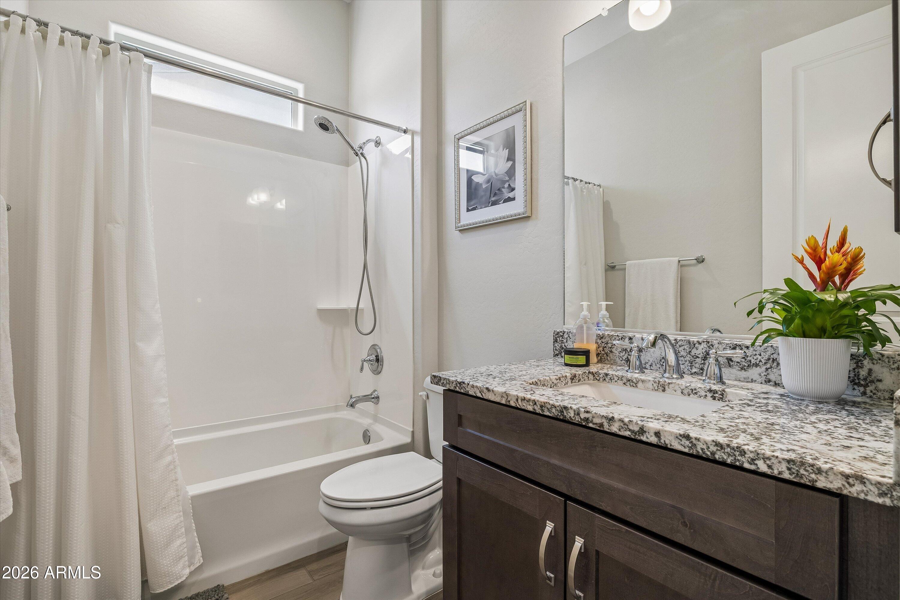 Bathroom with a white tub and shower beside a dark wood vanity with granite countertop.