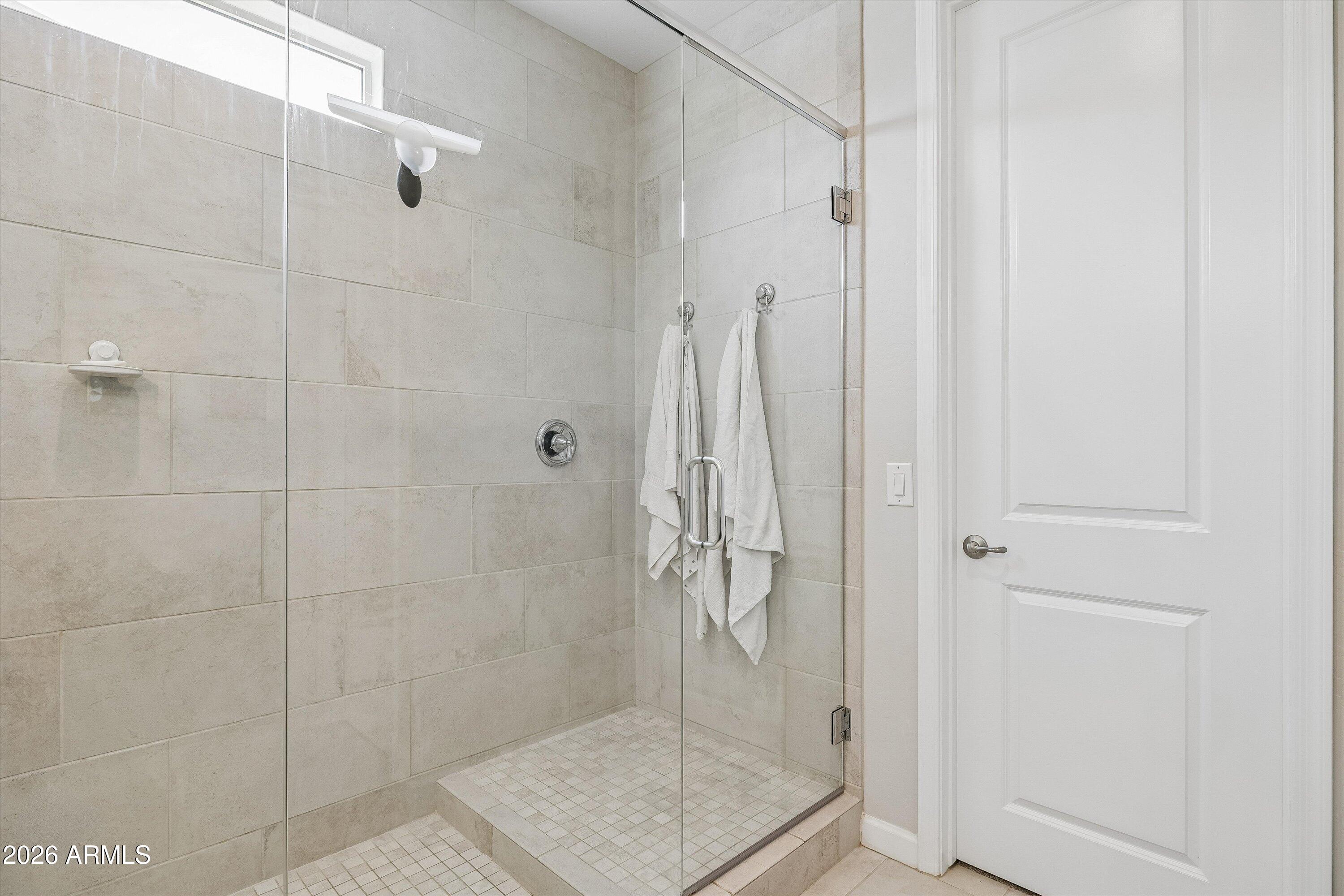 Walk-in shower with clear glass enclosure, beige tile walls, mosaic floor, and white towels.