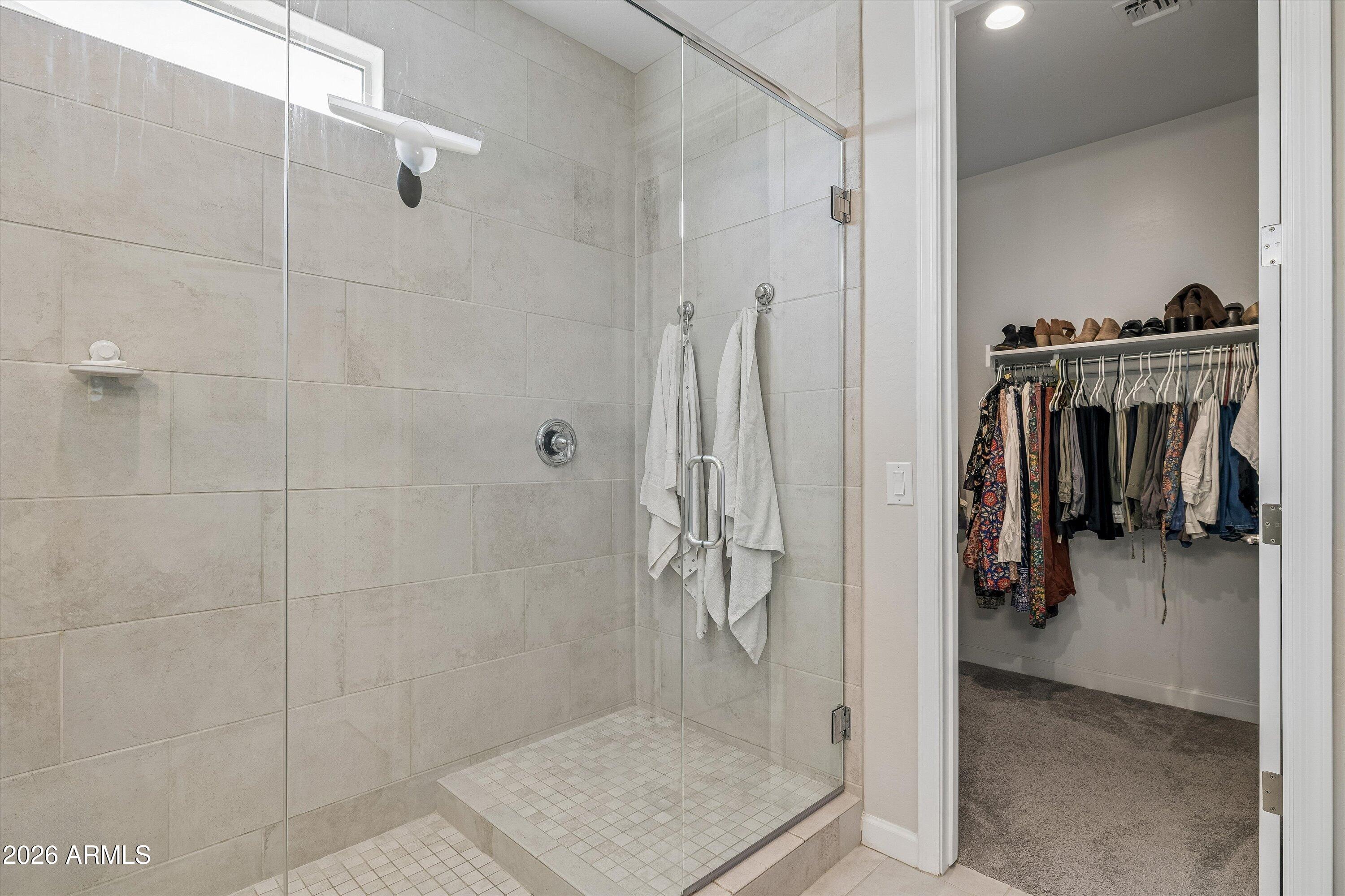 Bathroom with a glass-enclosed tiled shower beside an open walk-in closet.