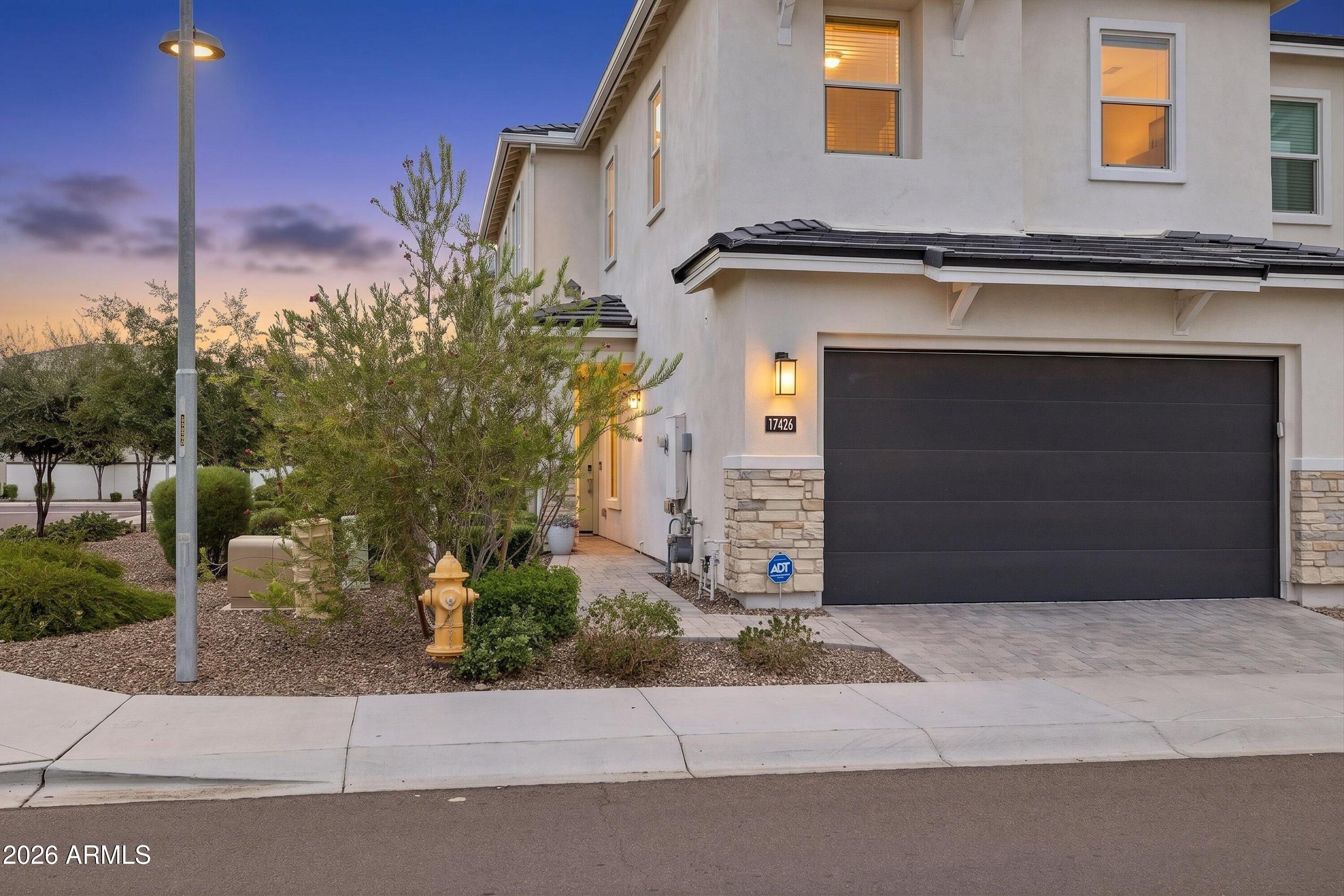 Two-story stucco home with a dark double garage, stone accents, and desert landscaping at dusk.