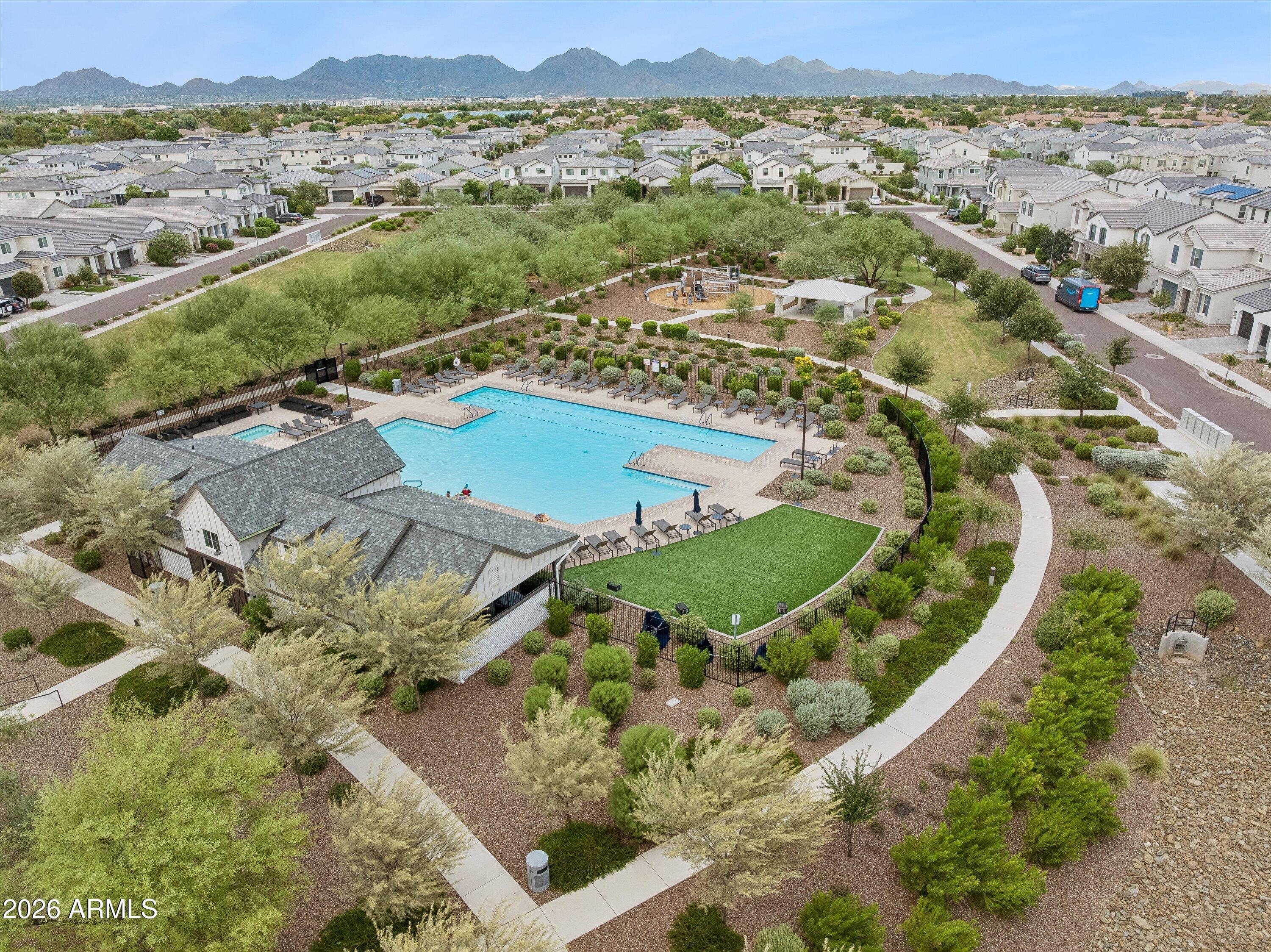 Aerial view of a community pool, clubhouse, landscaped paths, and mountain-backed neighborhood.