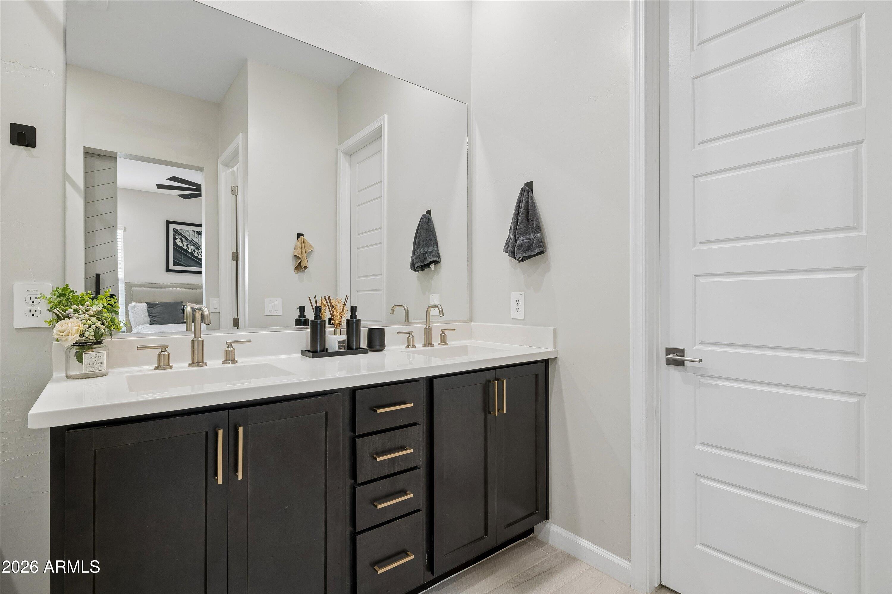Bathroom double vanity with dark cabinetry, brass hardware, white countertop, and large mirror.