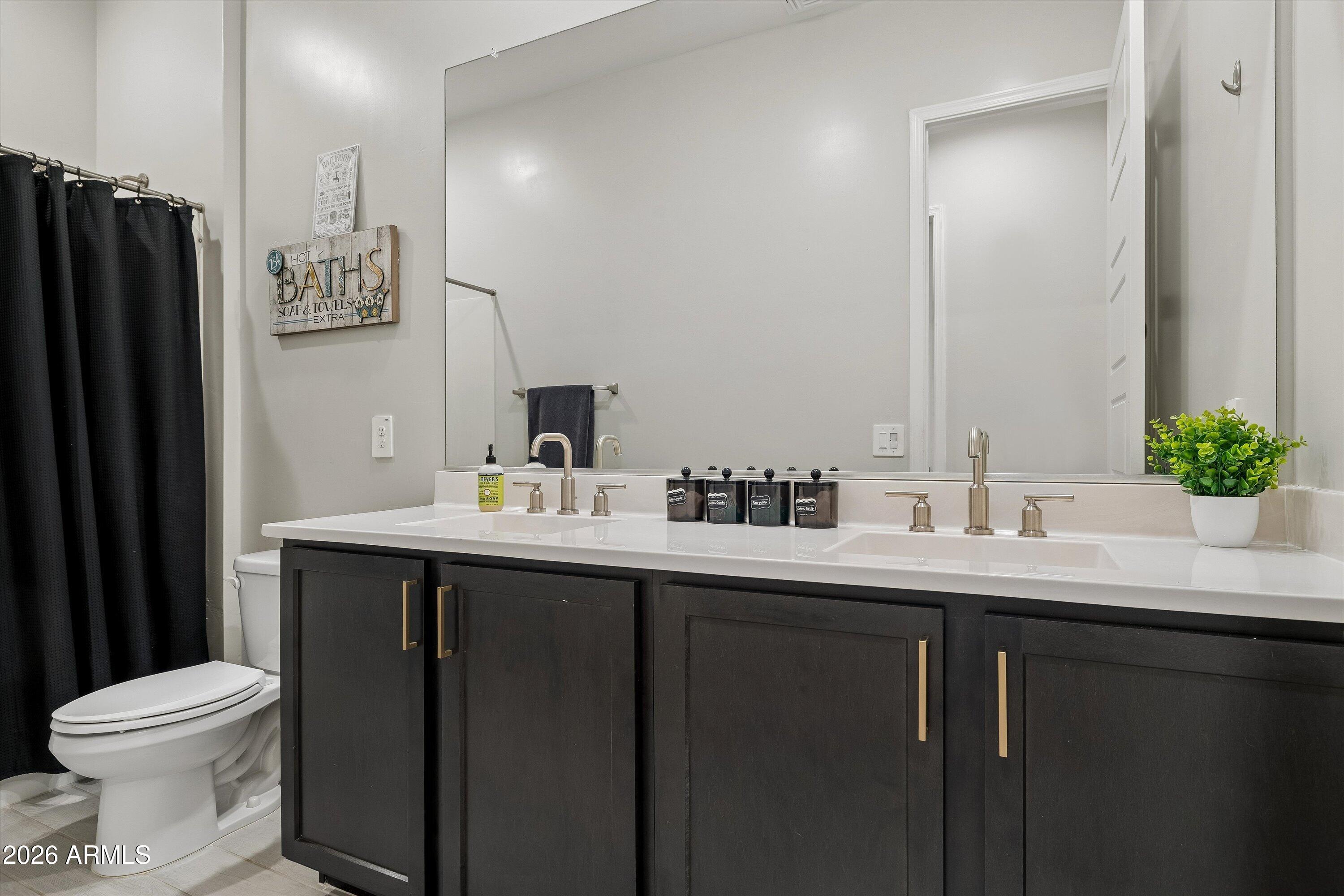 Bathroom with a dark double vanity, two sinks, a large mirror, and a black shower curtain.