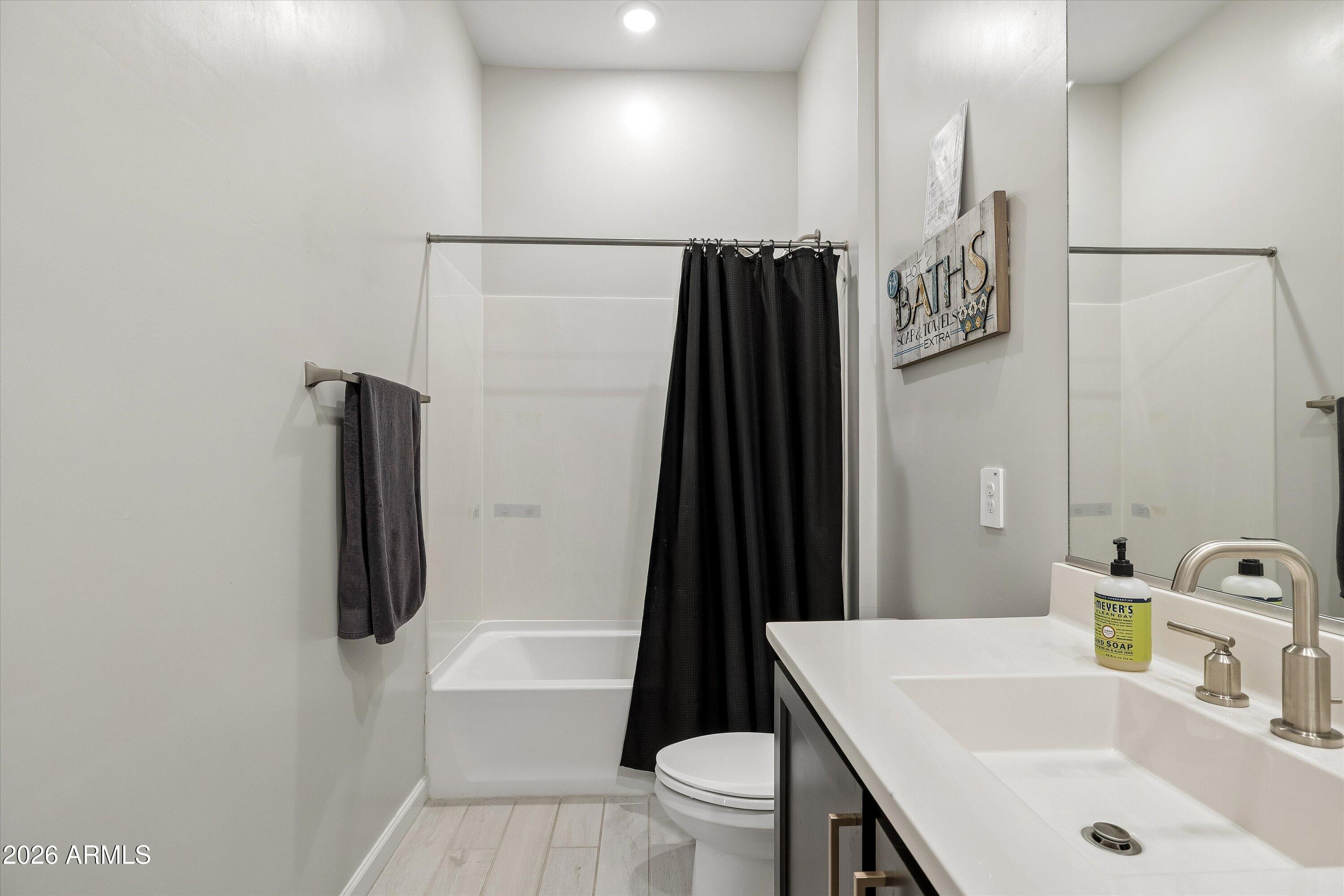 Bathroom with a white vanity, large mirror, and tub behind a black shower curtain.