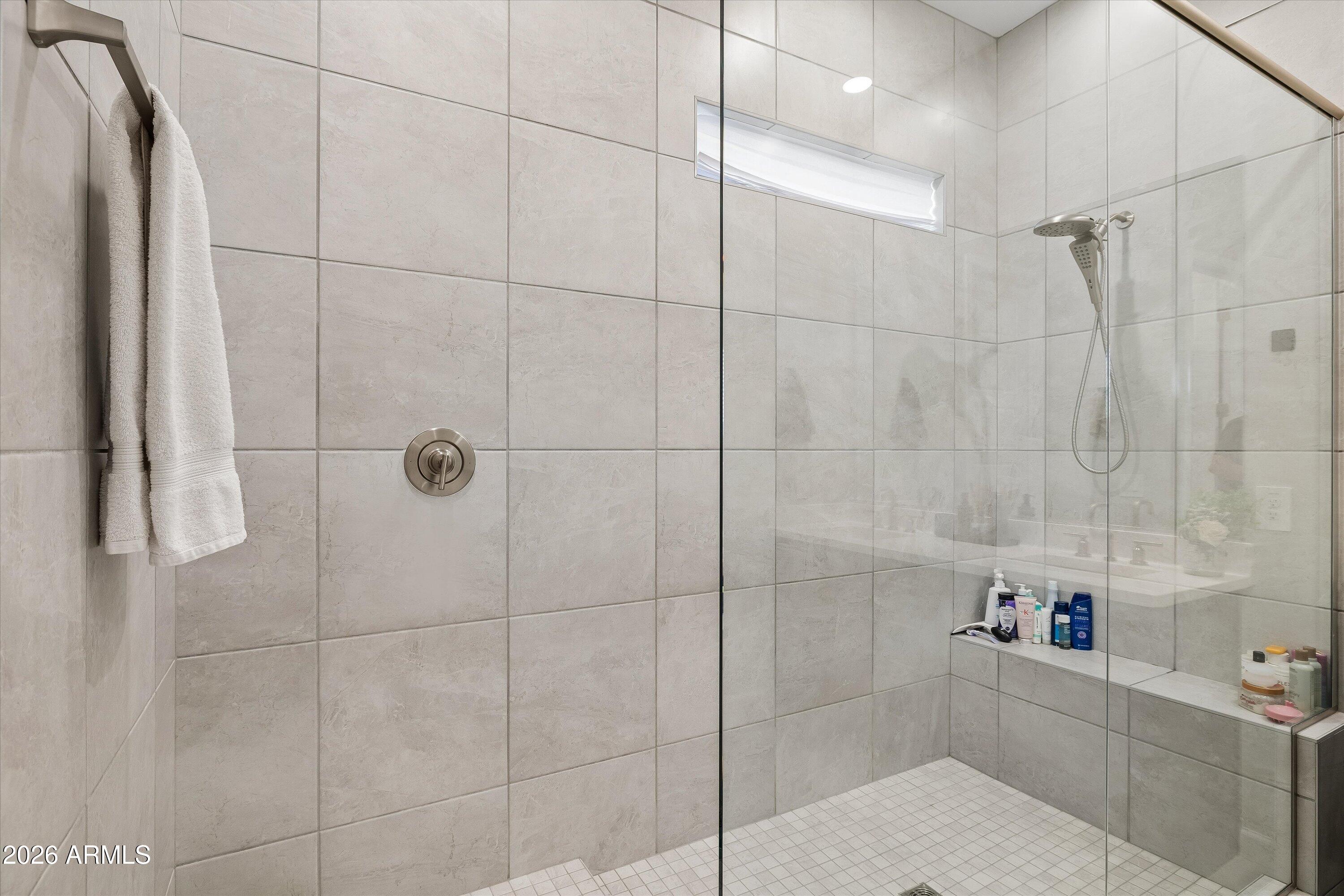 Tiled bathroom shower with a clear glass enclosure, handheld showerhead, and built-in ledge.