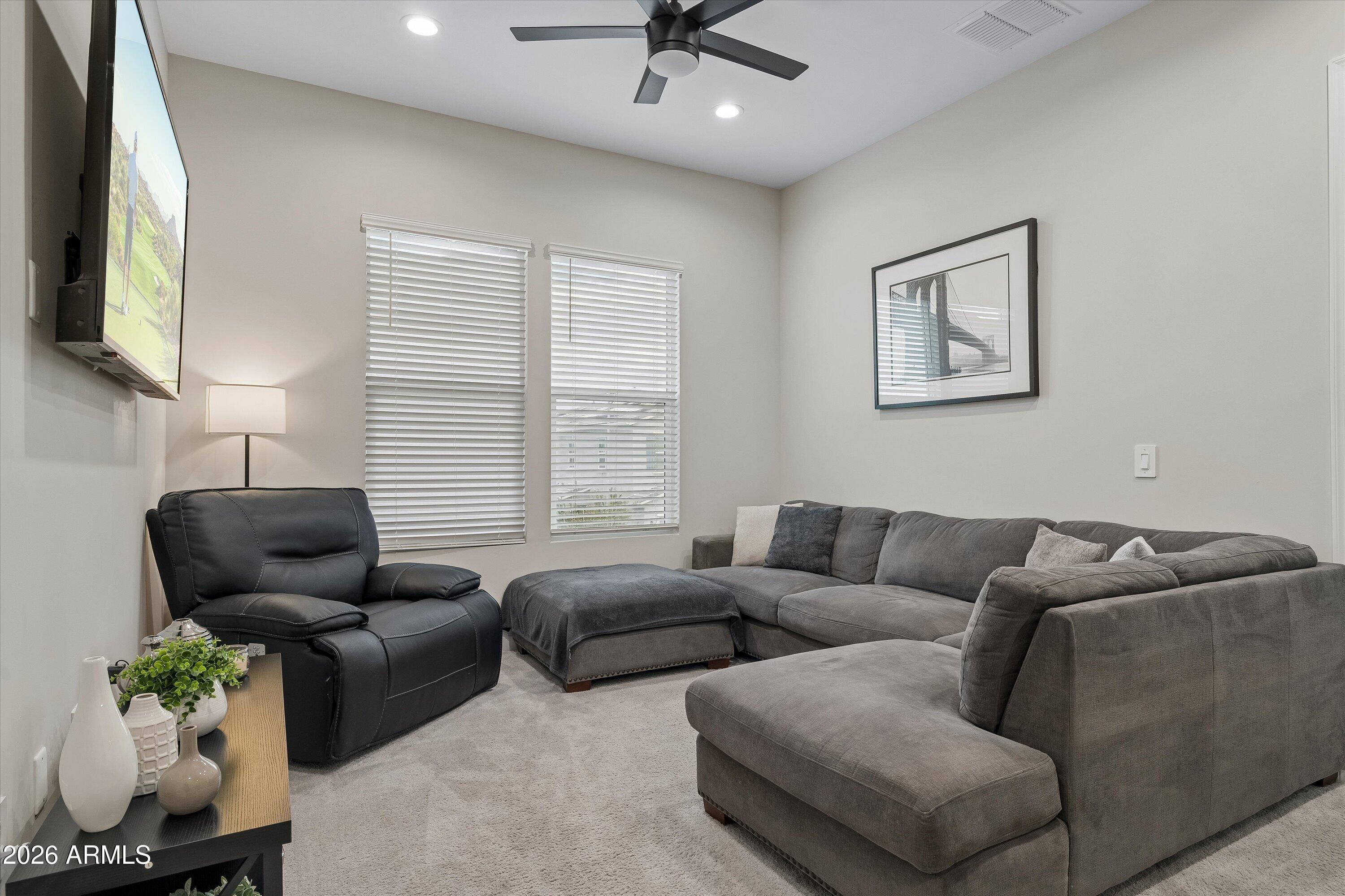 Furnished living room with a gray sectional, black leather recliner, and two windows with white blinds.