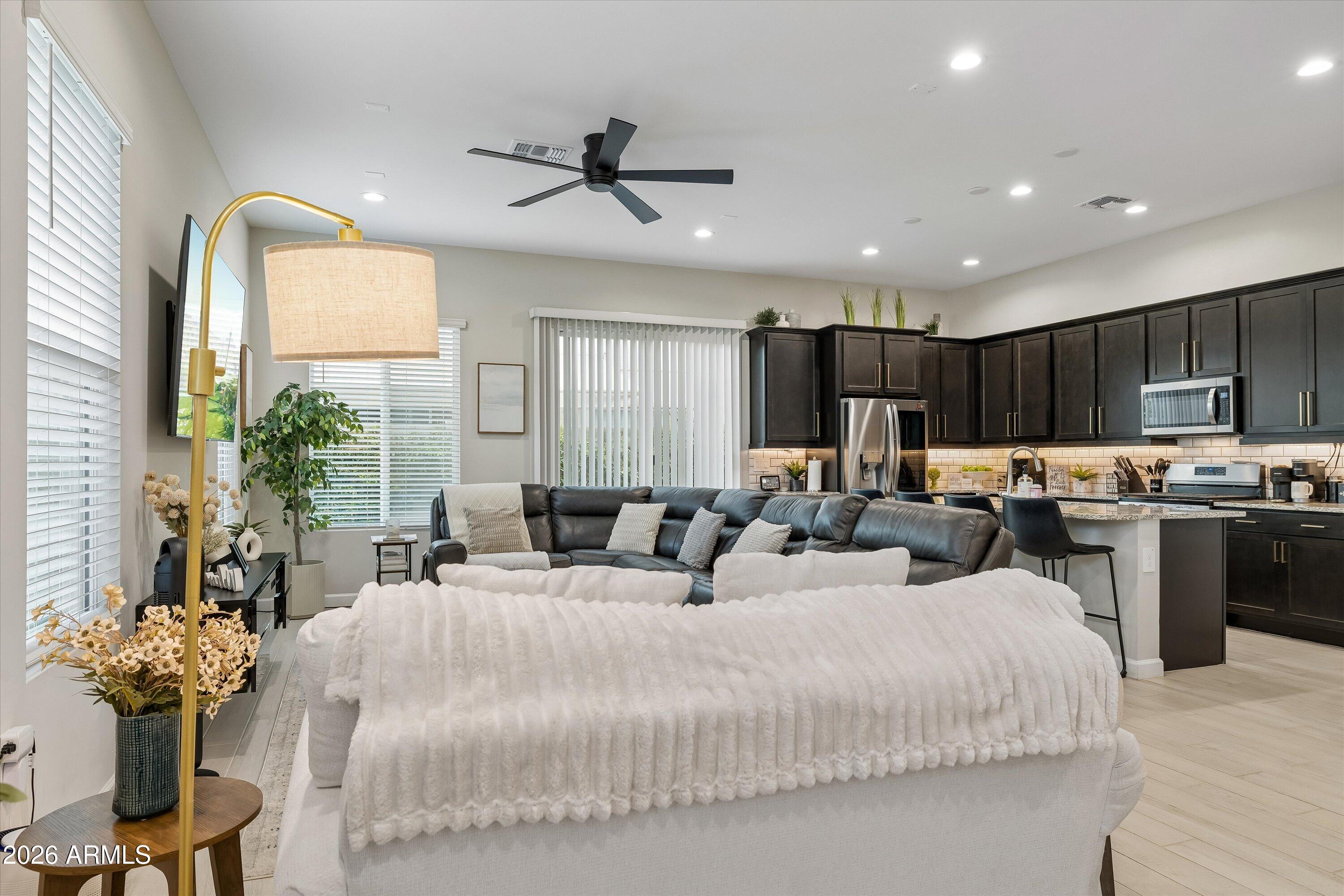 Open-plan living room and kitchen with a black sectional, dark cabinets, and a stone island.