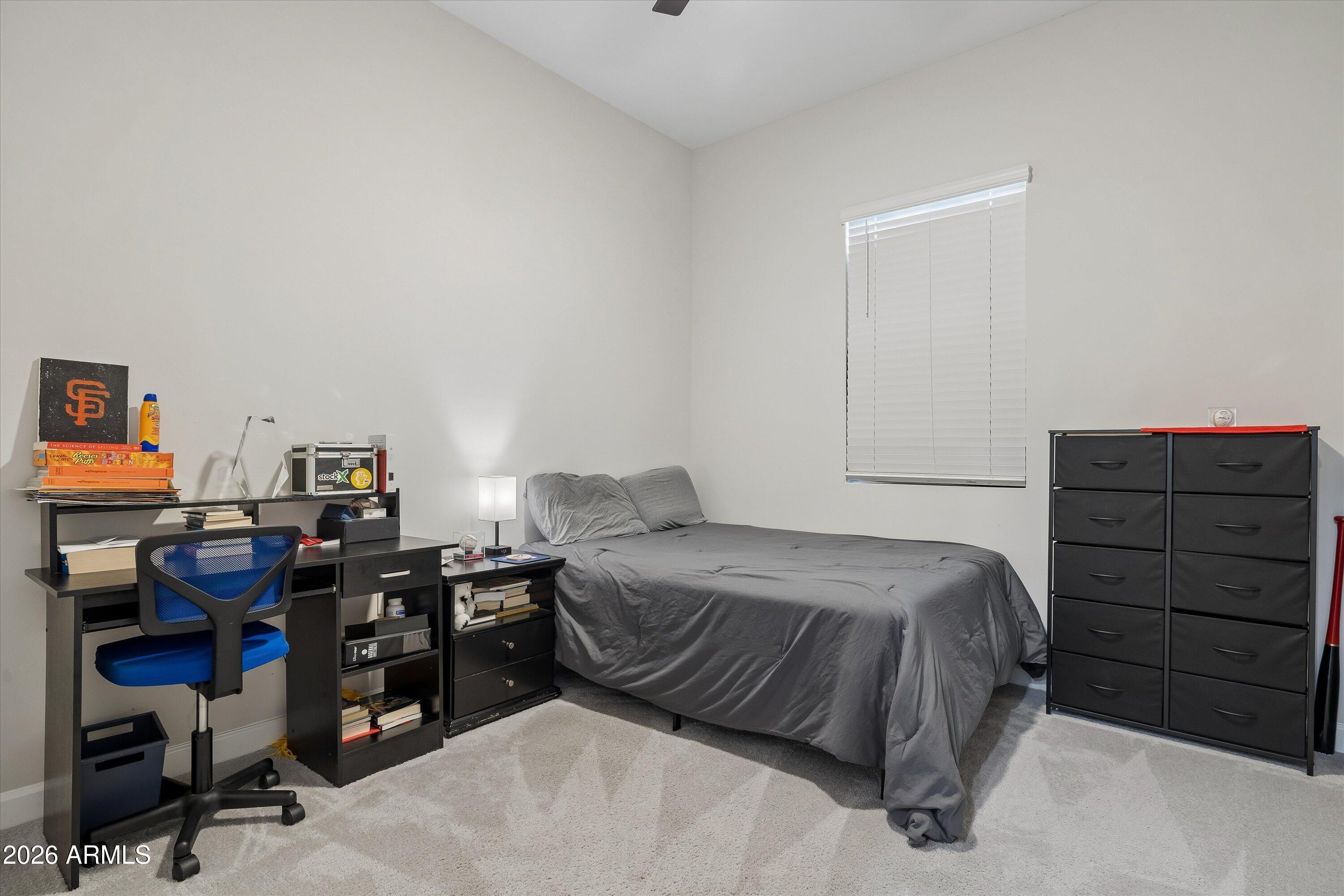 Bedroom with a gray-covered bed, black dresser, and desk with a blue chair.