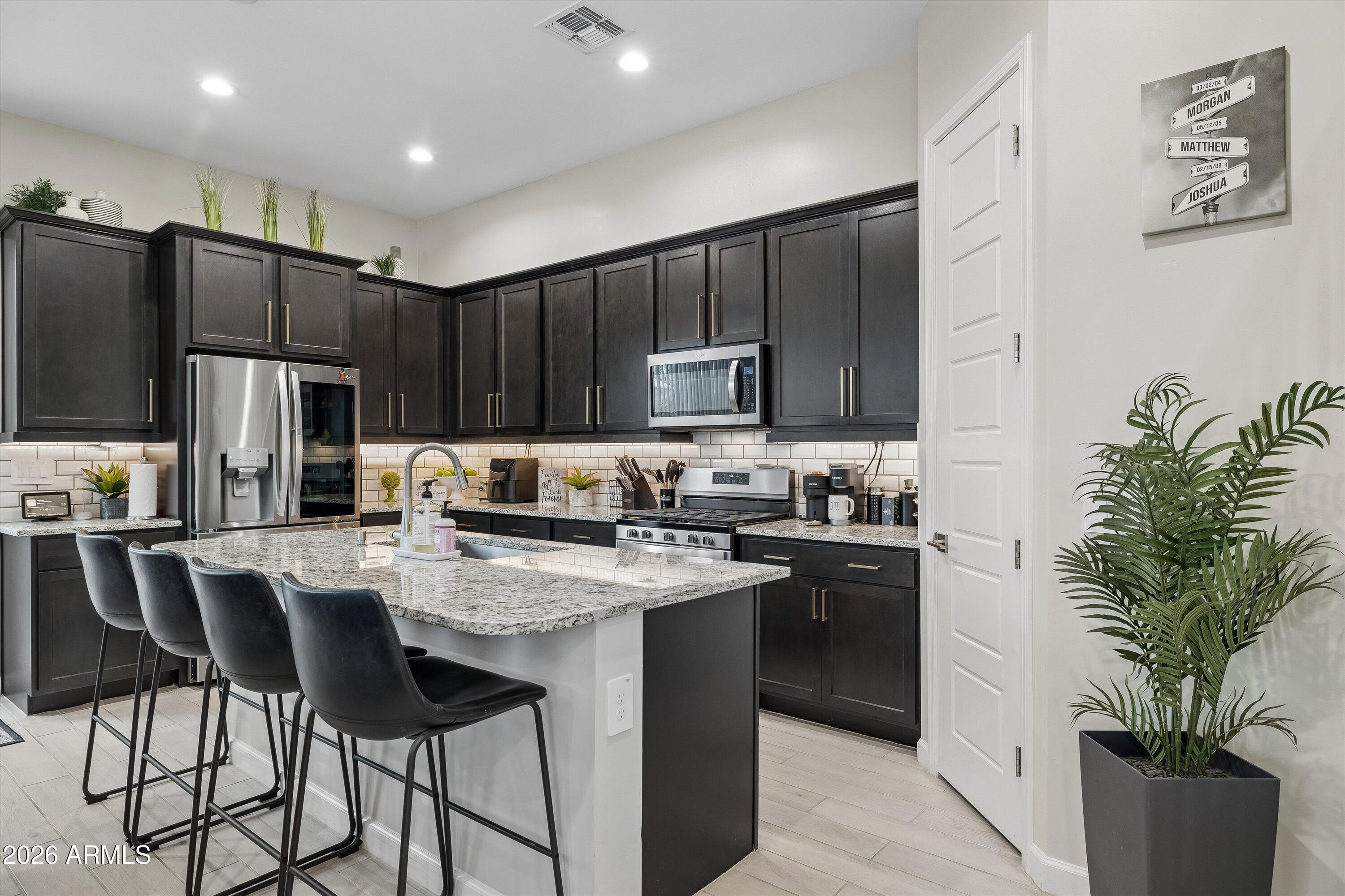 Kitchen with dark cabinets, stainless steel appliances, and a large stone island with bar stools.