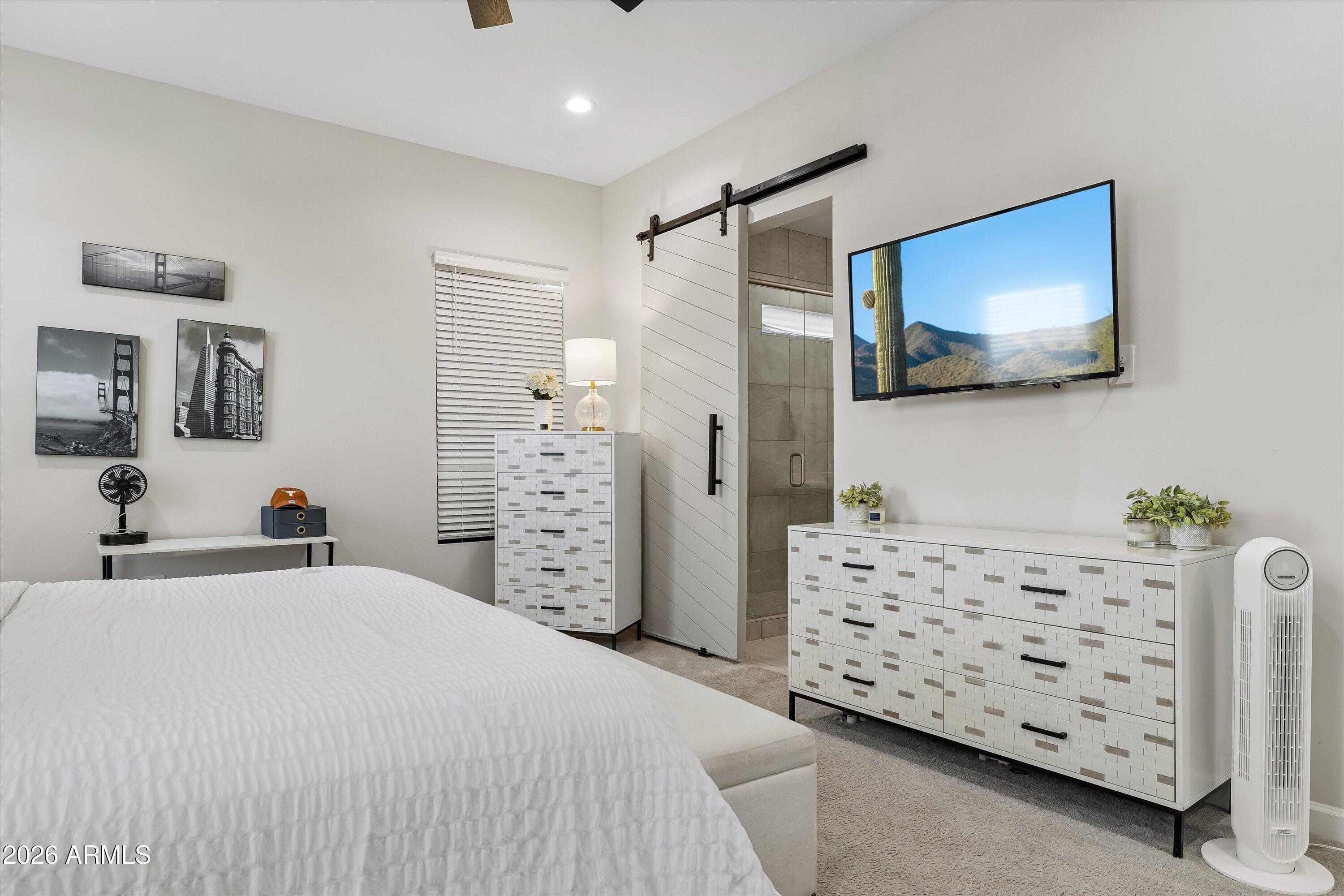 Furnished bedroom with patterned white dressers and an open sliding barn door to a tiled shower.