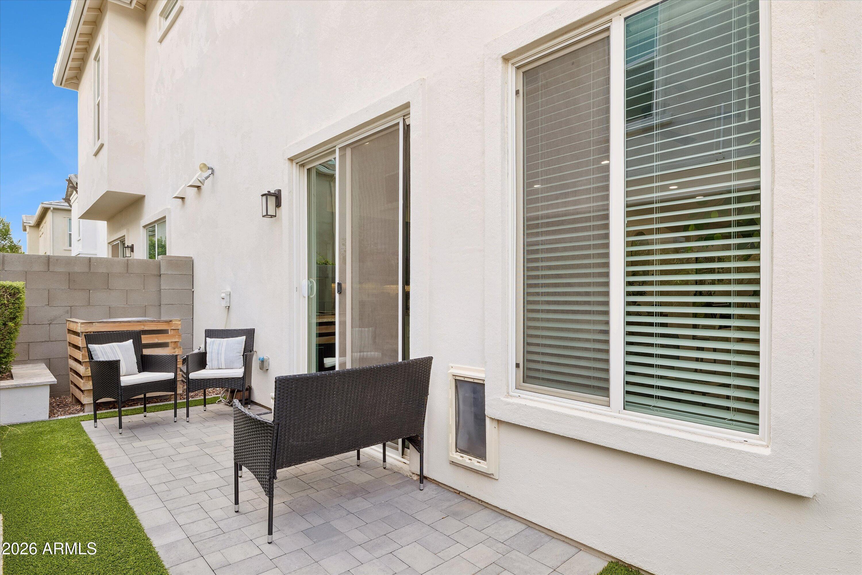 Furnished patio with gray pavers, black wicker seating, and green turf beside a white stucco home.