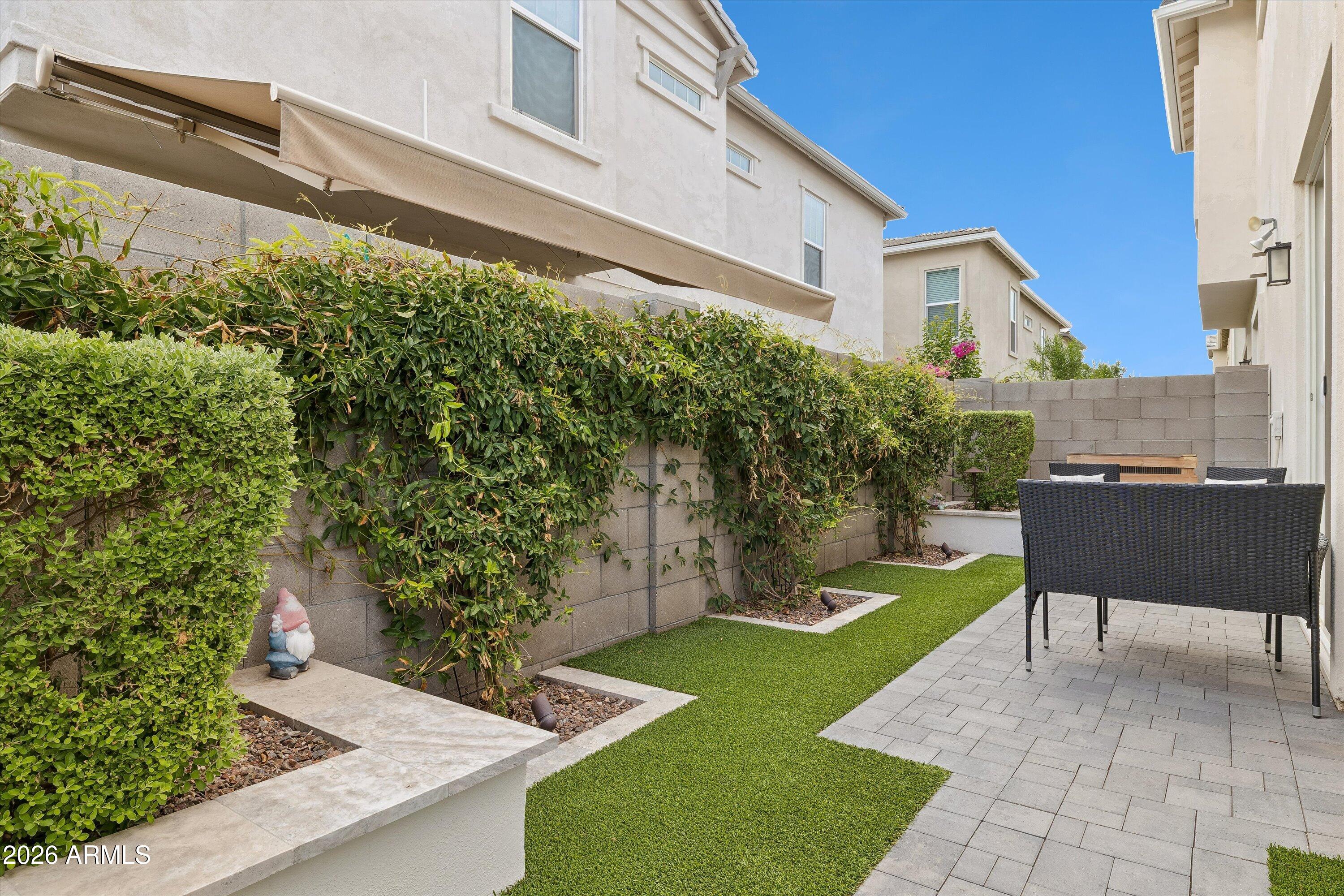 Enclosed townhouse patio with artificial turf, vine-covered walls, pavers, and black wicker seating.