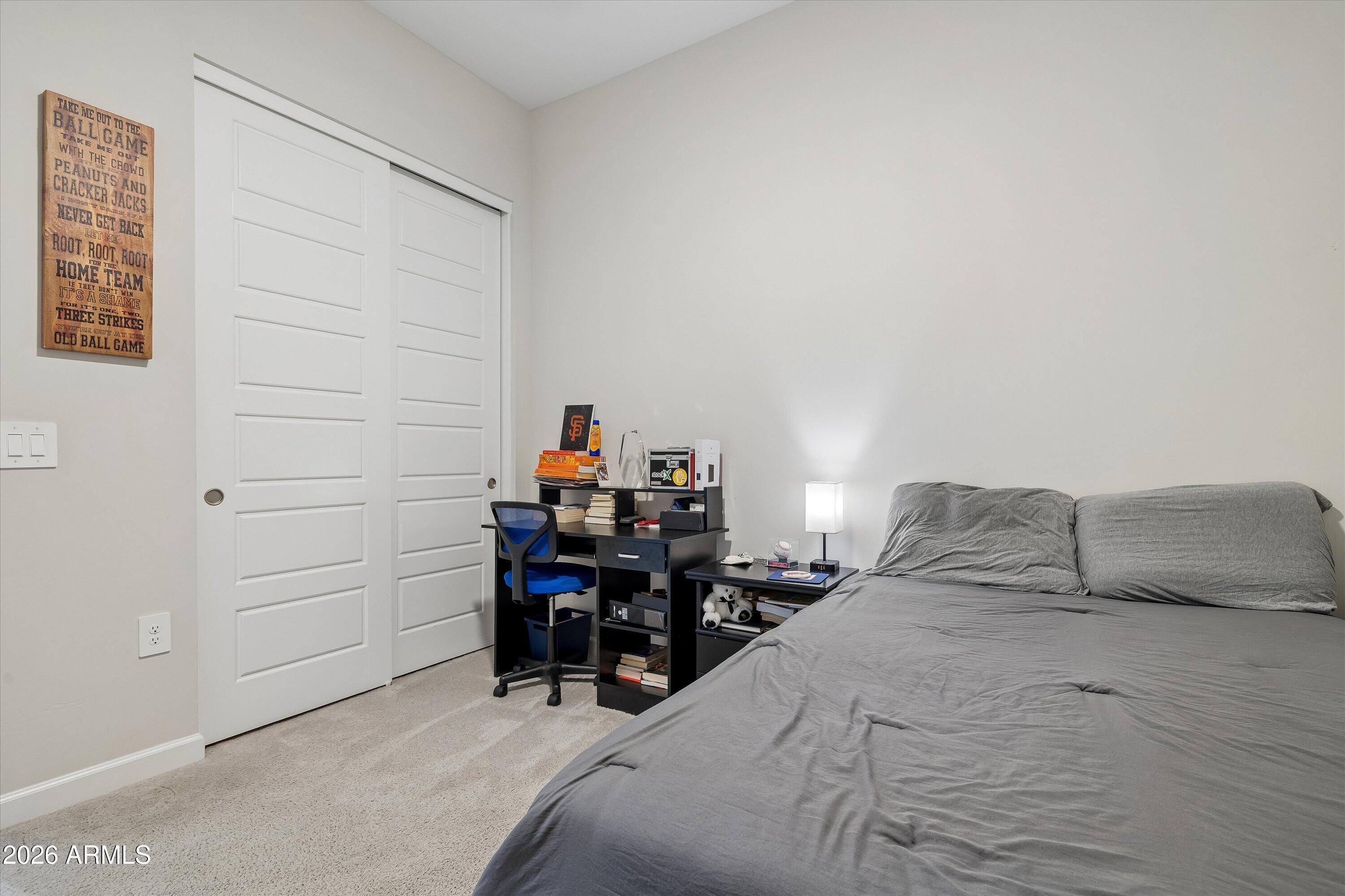 Bedroom with a gray bed, black desk and blue chair, white sliding closet doors, and baseball-themed wall sign.
