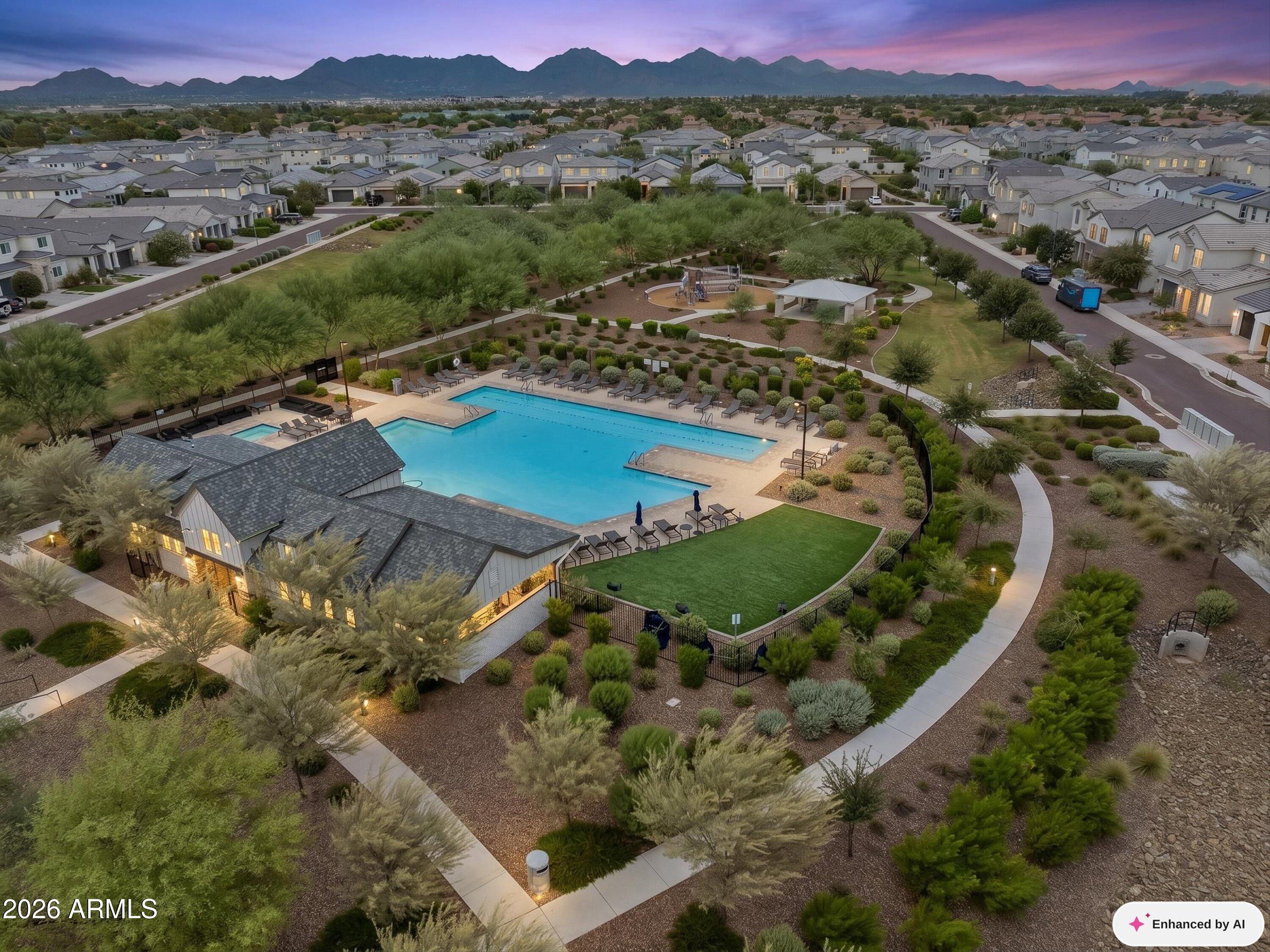 Aerial view of a community pool and clubhouse, with homes and mountains beyond.