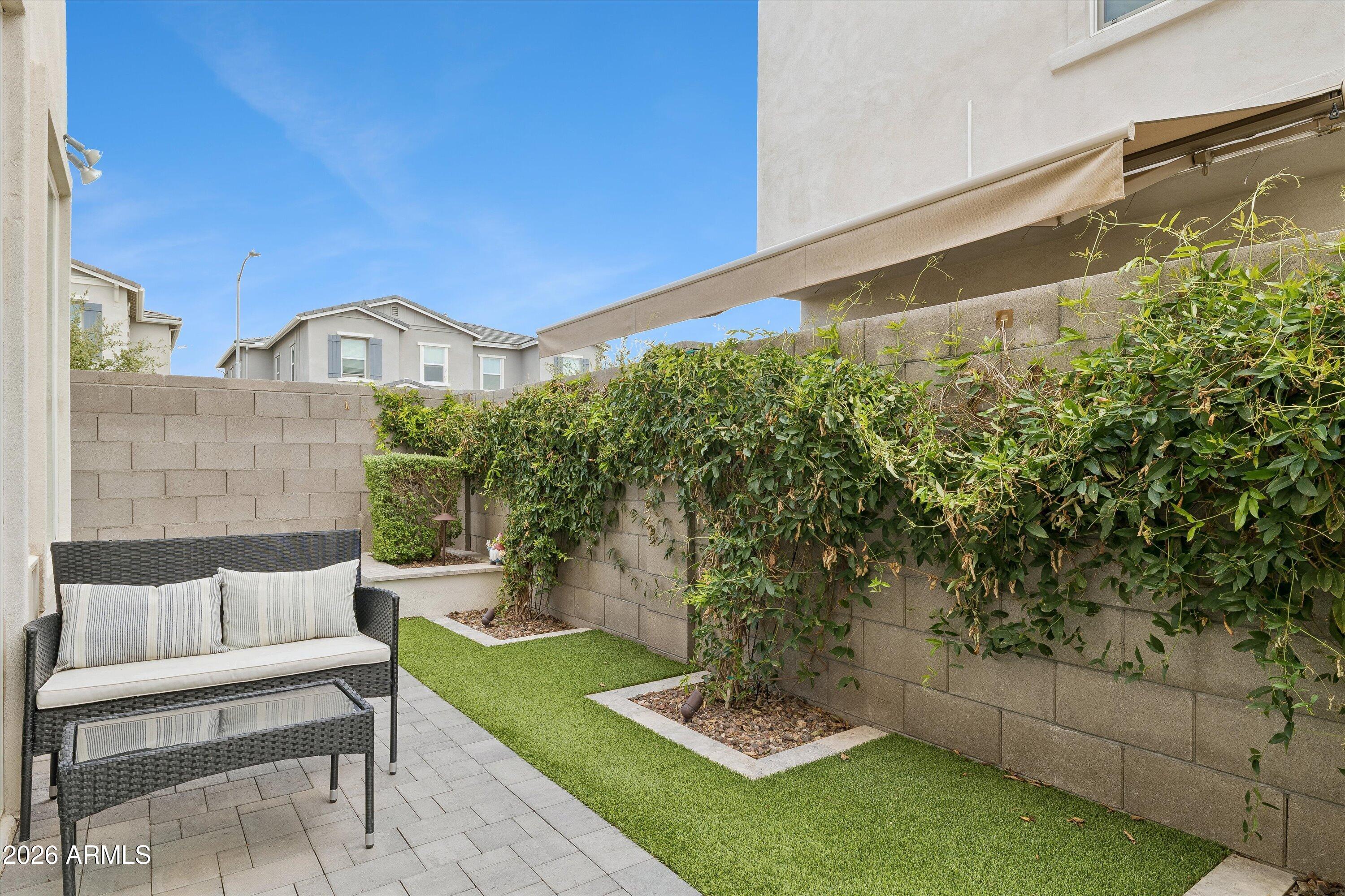 Backyard patio with wicker seating, artificial turf, vine-covered walls, and a retractable shade canopy.