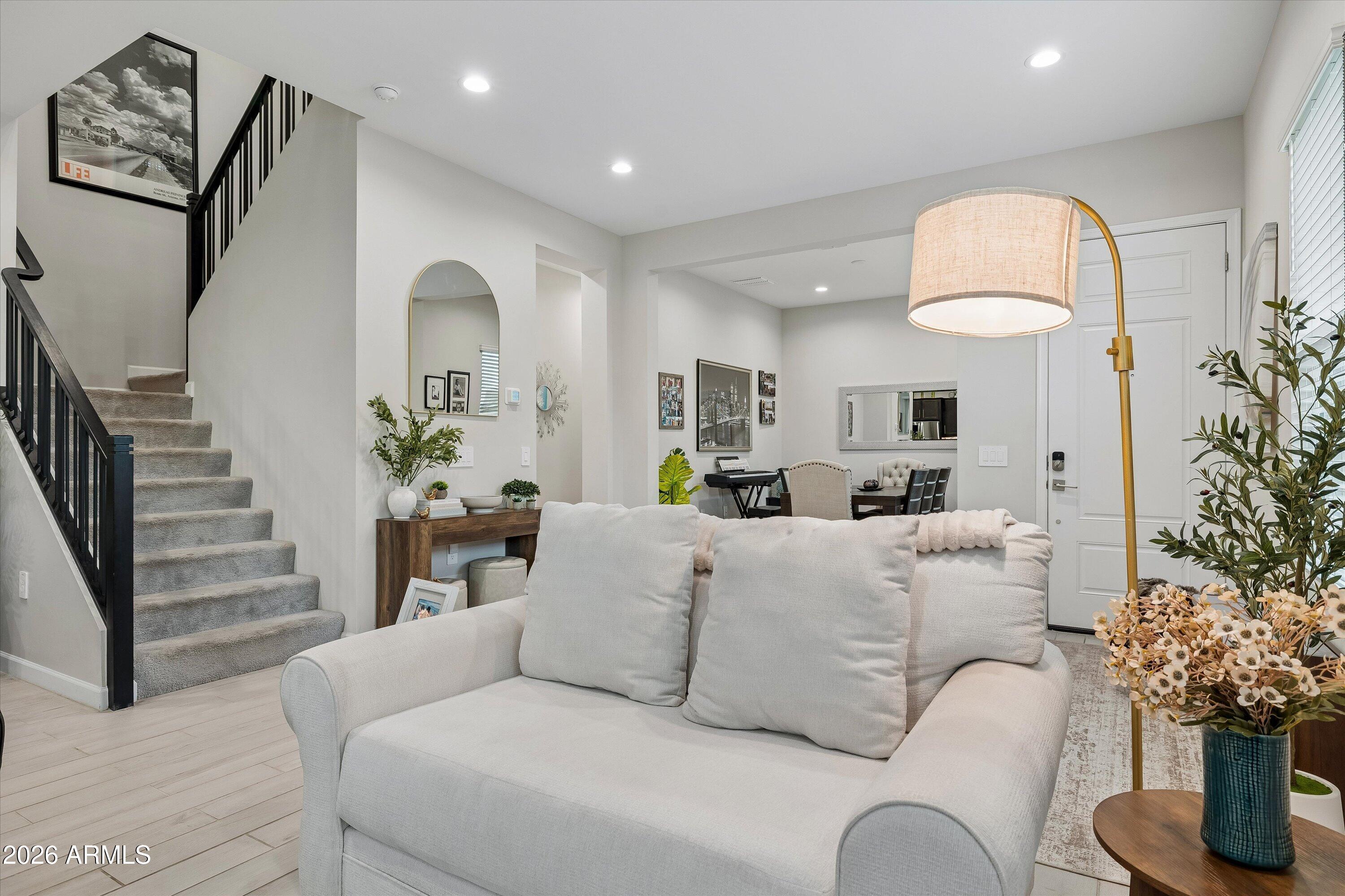 Living room with a white sofa, carpeted staircase with black railing, and dining area beyond.