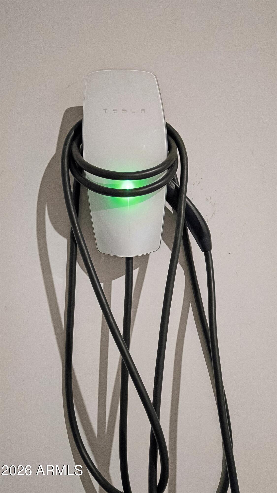 Tesla wall charger with a glowing green indicator and coiled charging cable.