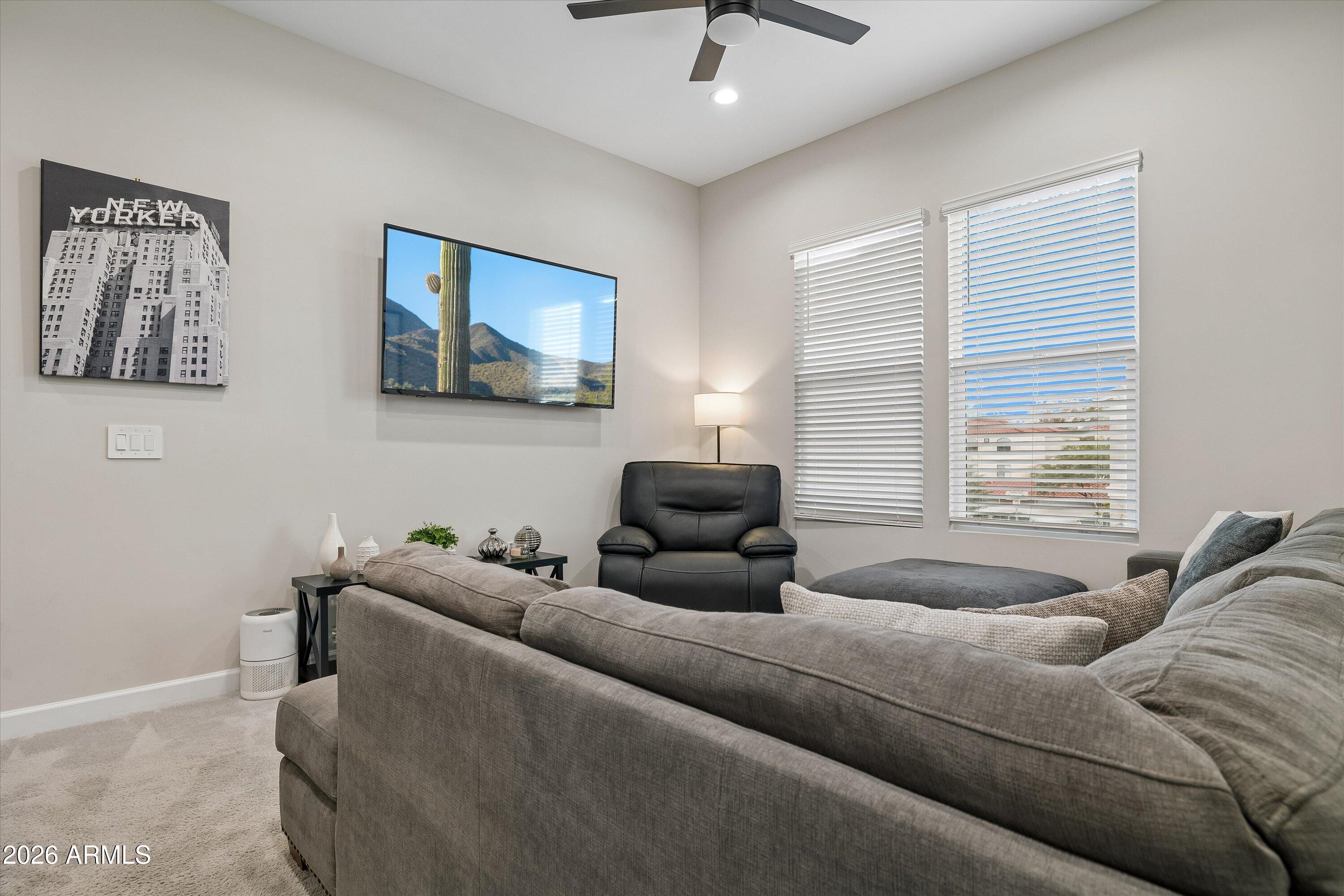 Living room with a gray sectional, black recliner, wall-mounted TV, and windows with white blinds.