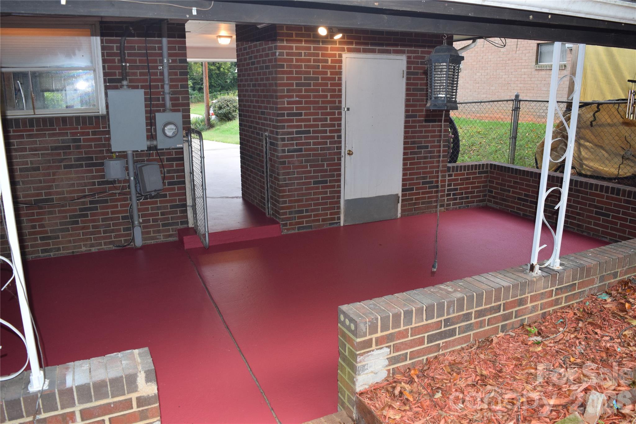 Covered brick patio with a red floor, low brick walls, and a chain-link gate.