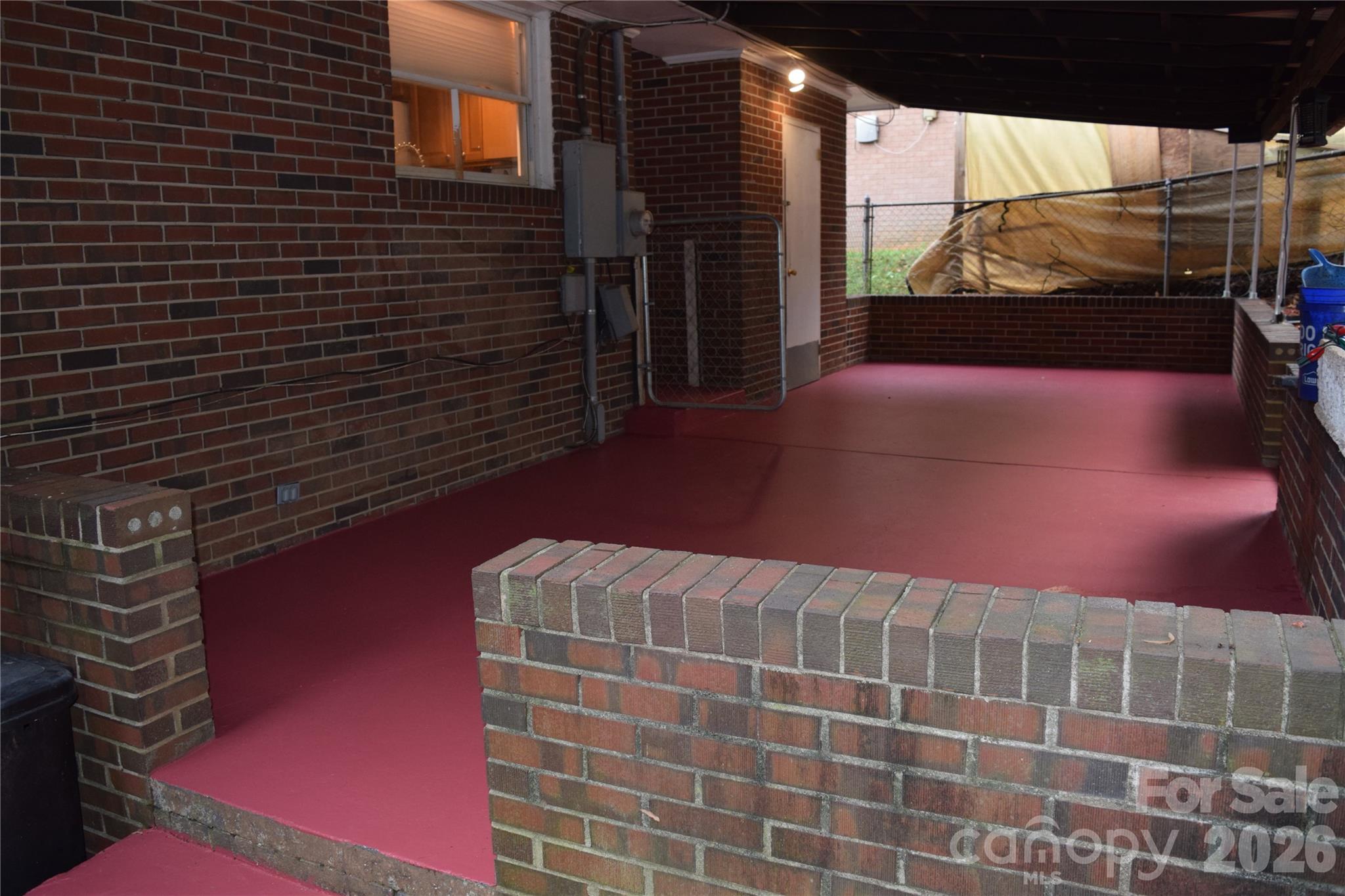 Covered brick patio with a red floor and low brick walls.