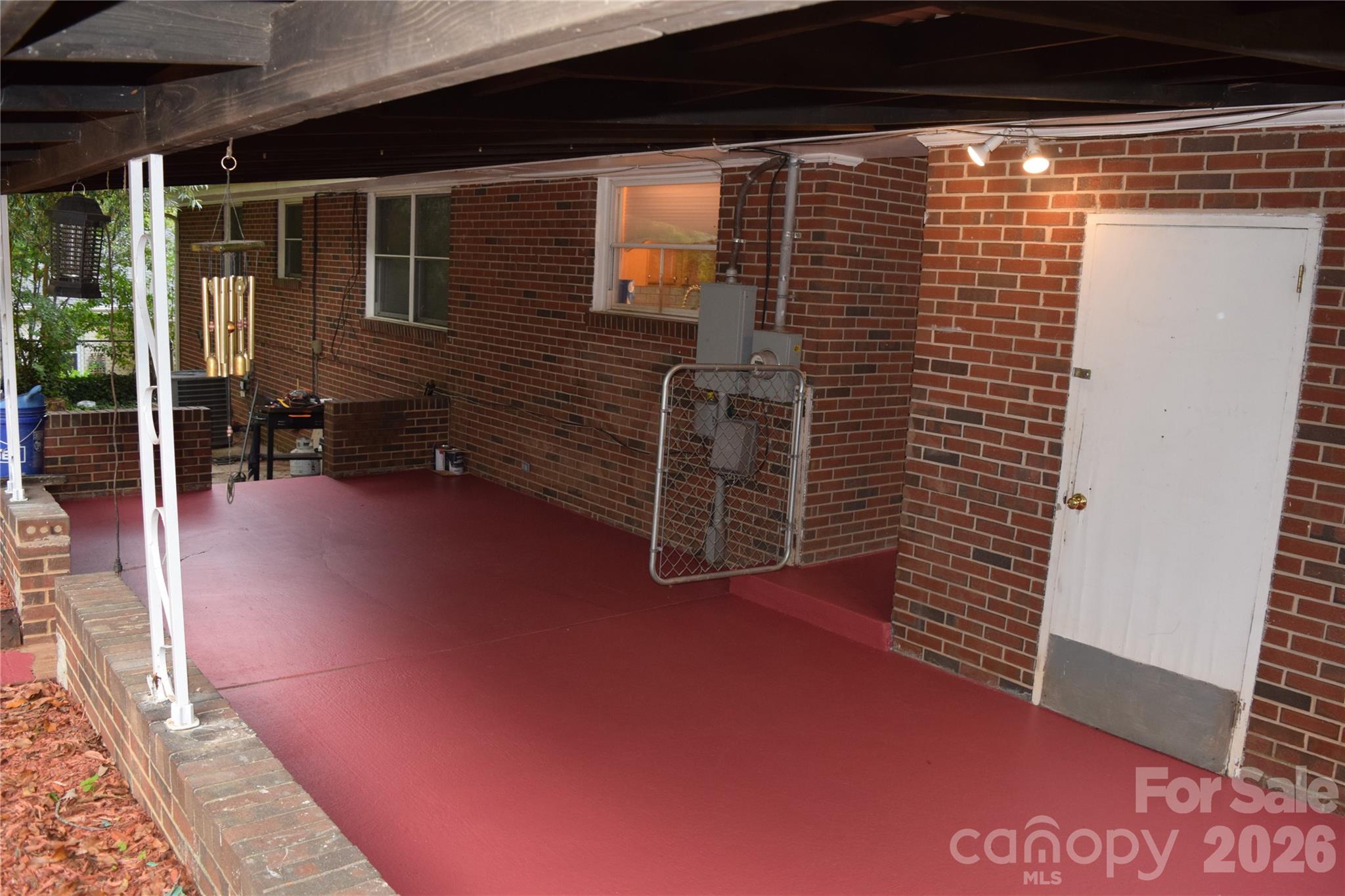Covered patio with red flooring, brick walls, and white support posts.