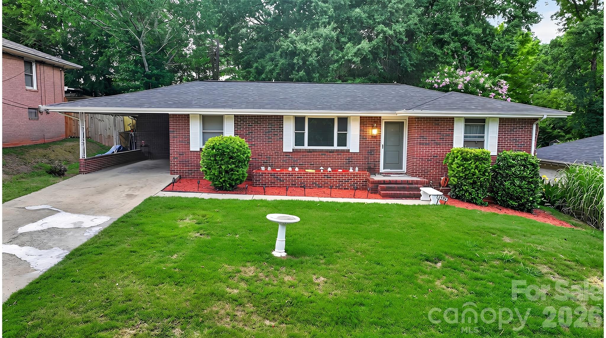 Red brick ranch house with a covered carport, front steps, and broad green lawn.