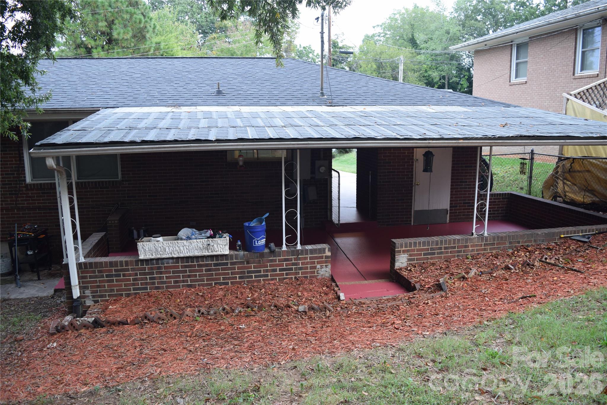 Brick house rear patio with a broad metal roof and red-painted floor.