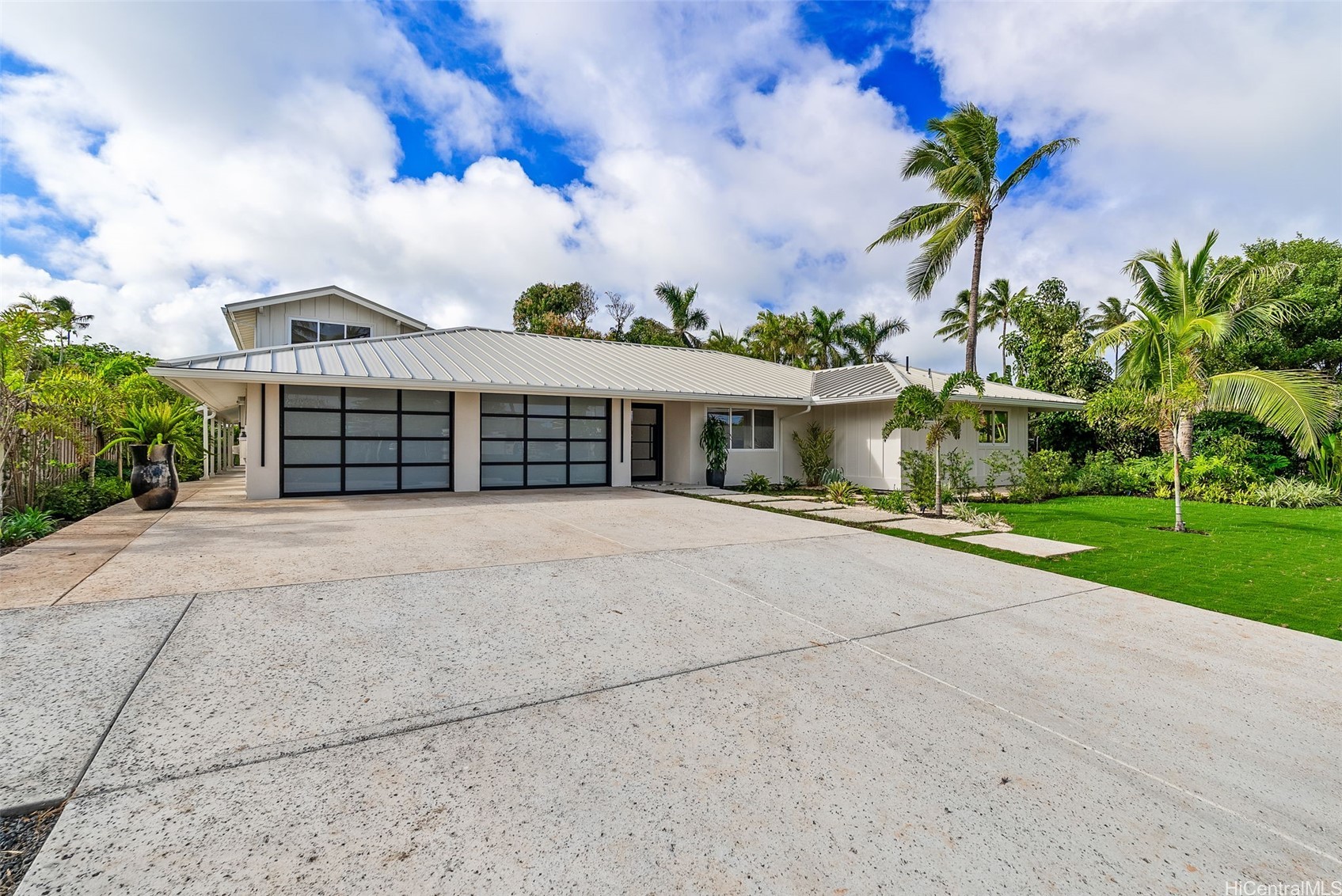 Single-story home with two garage doors, a broad concrete driveway, and tropical palm landscaping.