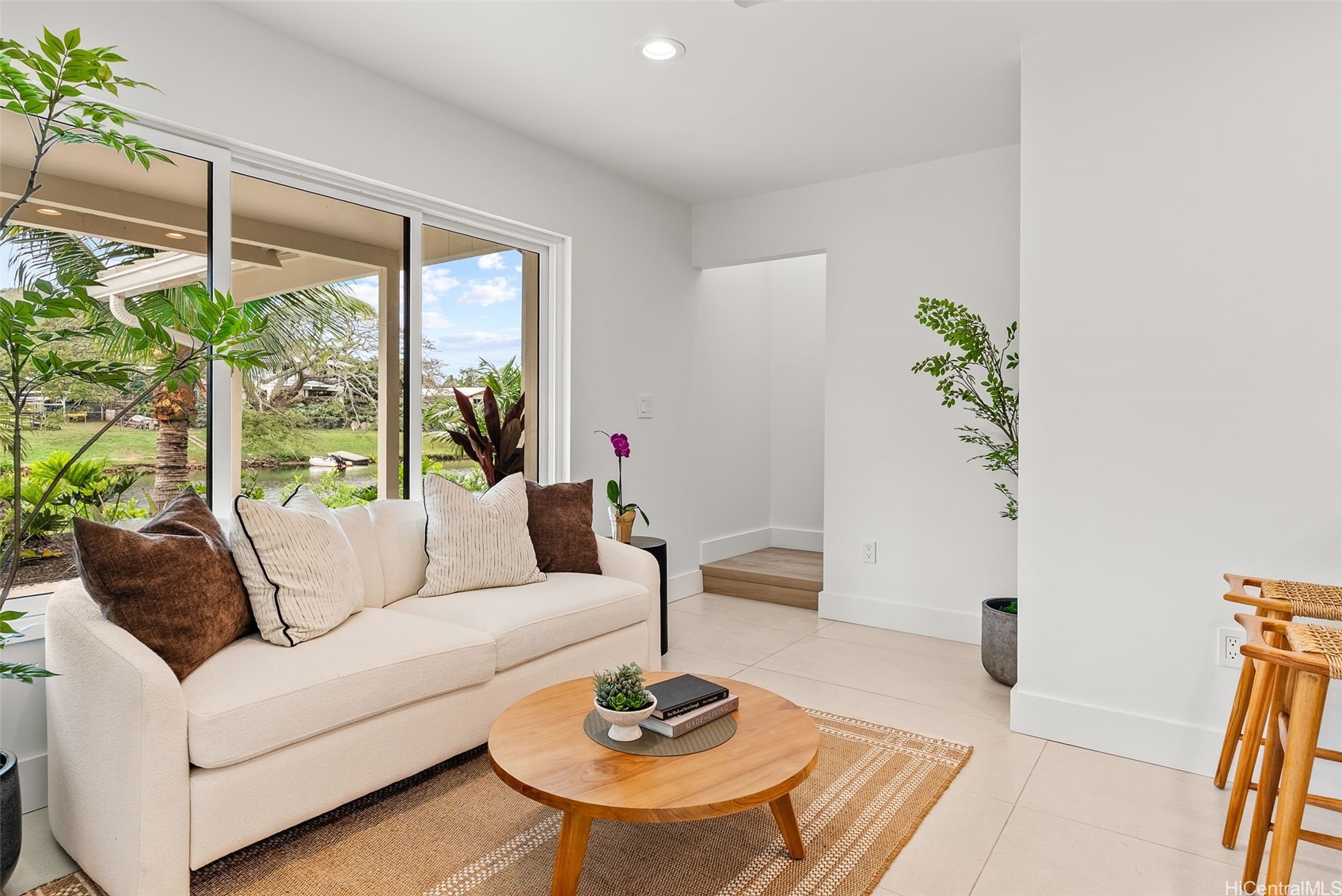 Staged living room with a white sofa, wood coffee table, and sliding doors overlooking a garden and waterway.