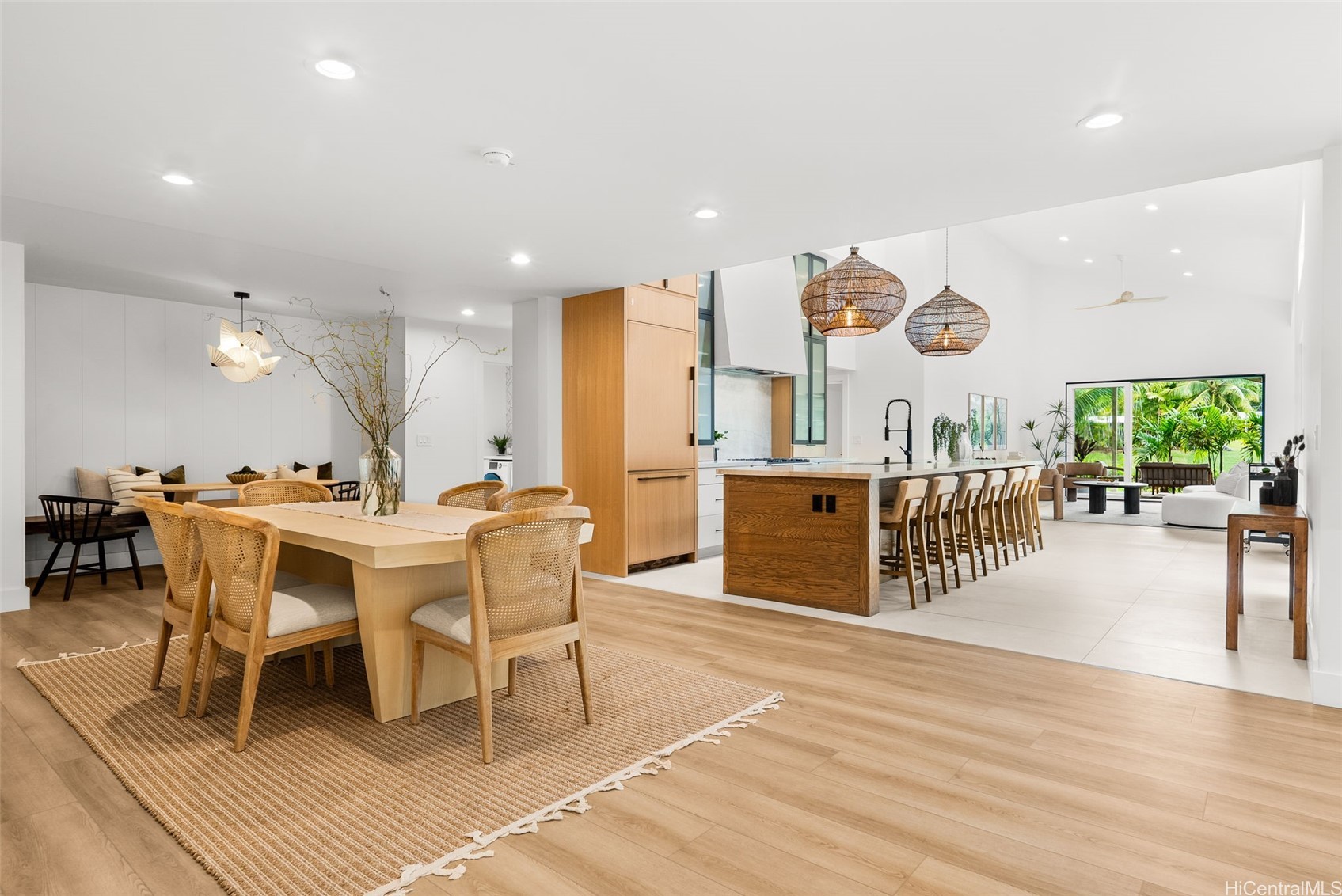 Open-plan kitchen and dining area with a long island, woven pendants, and garden-facing glass doors.