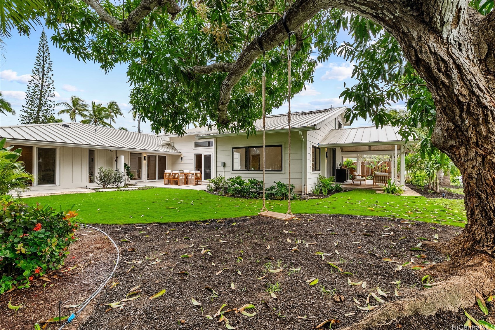 Home with a covered patio, broad green lawn, and a swing hanging from a large shade tree.