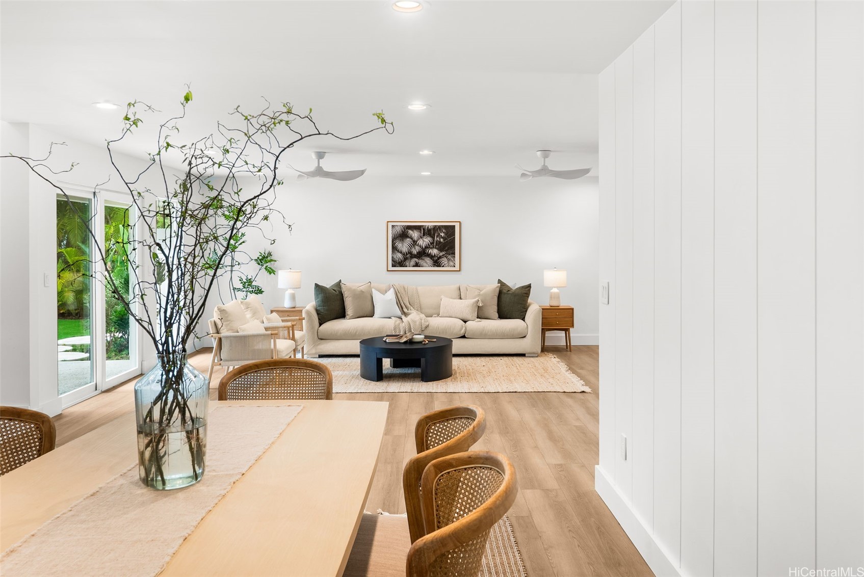 Open-plan living and dining area with a cream sofa, cane chairs, and sliding doors to greenery.