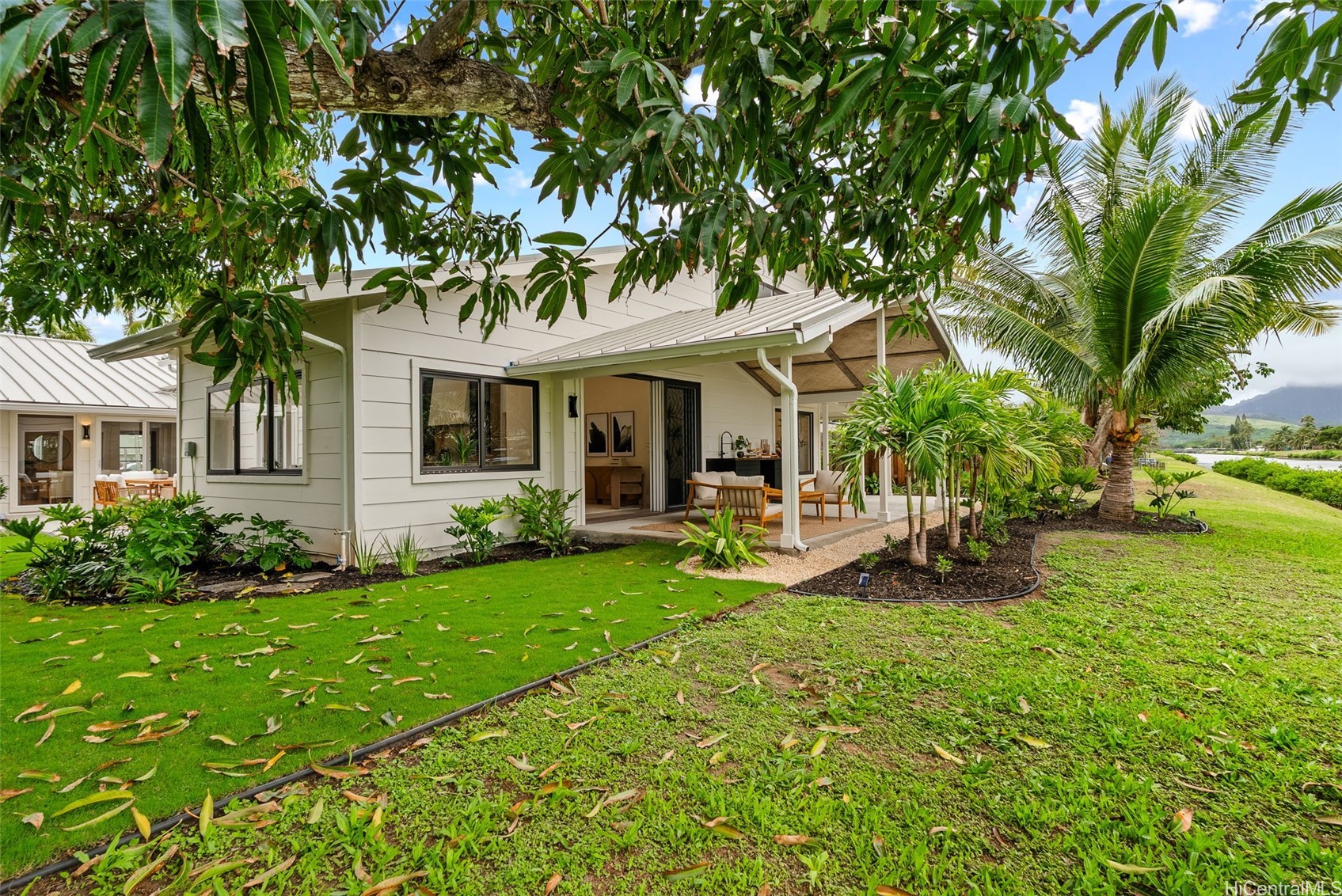 Single-story home with a covered lanai, tropical landscaping, and a mountain in the distance.